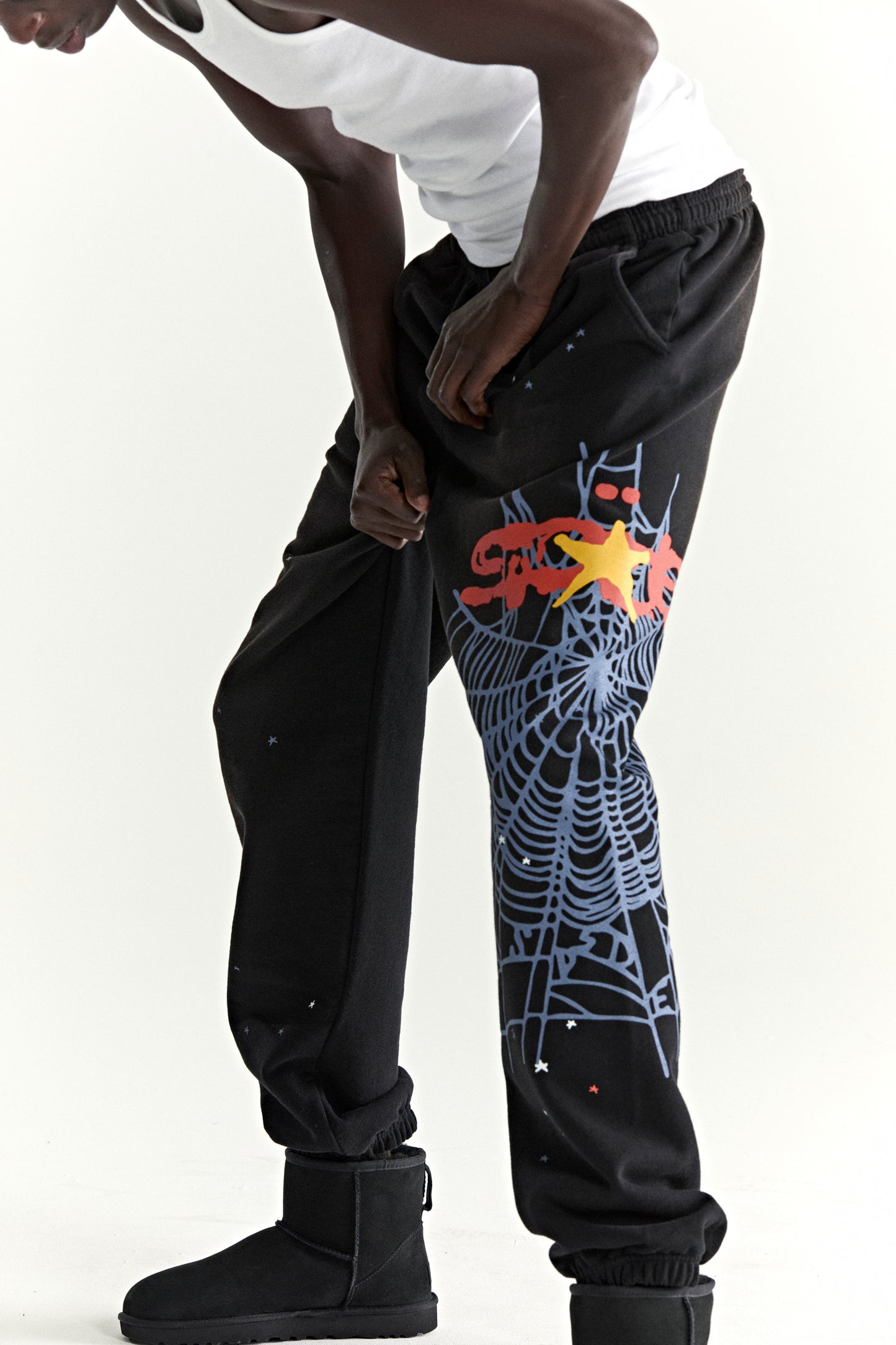 Black cotton fleece sweatpants with red, yellow, and blue SP5DER web graphic and scattered stars.