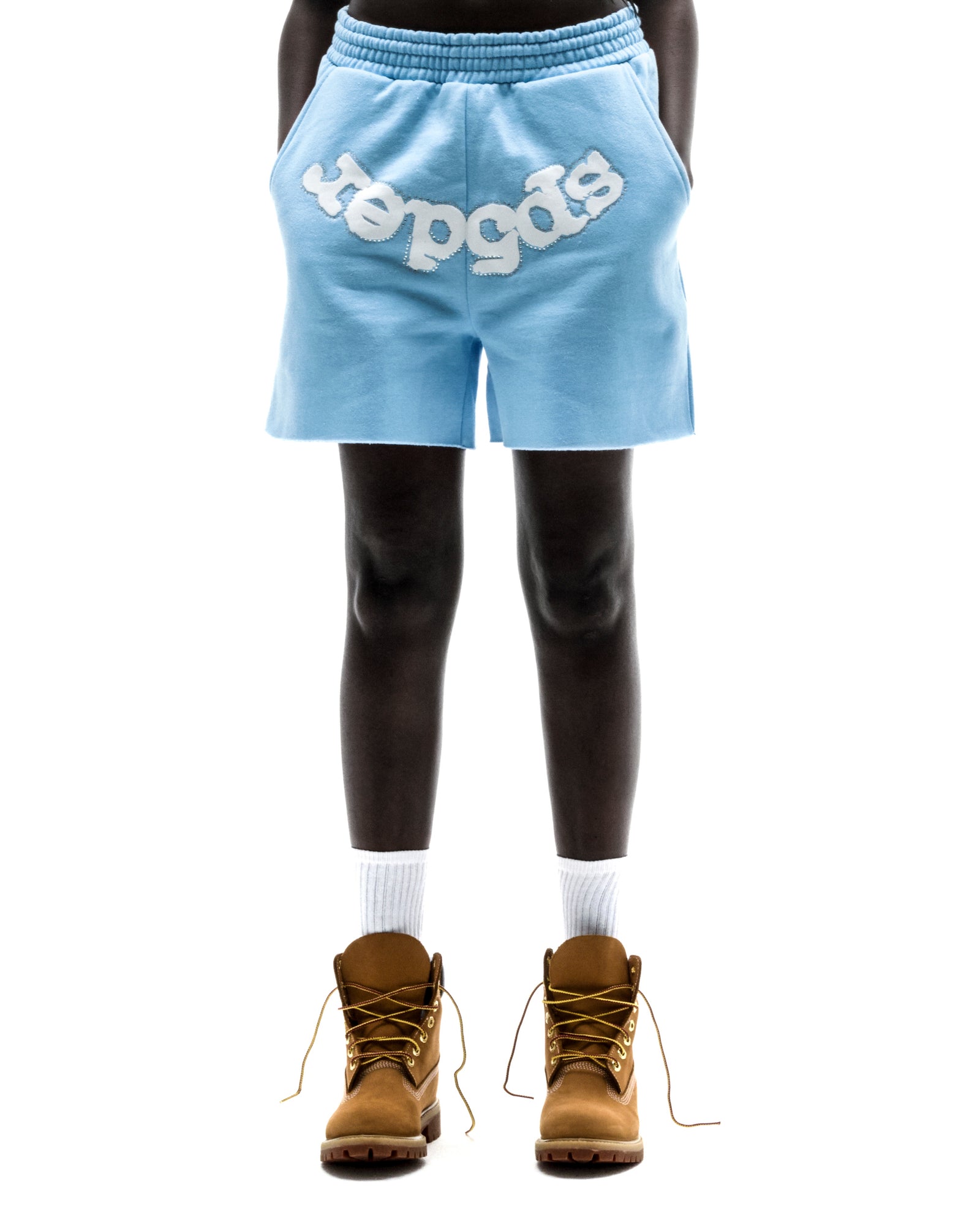 Model wearing light blue OG WEB SWEATSHORT with "SP5DER" text, raw hem, and brown boots.