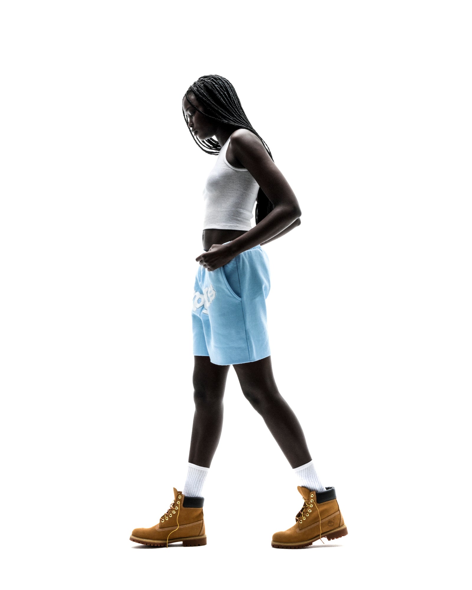 Model in light blue OG WEB SWEATSHORT with "SP5DER" print, white tank top, and tan boots.