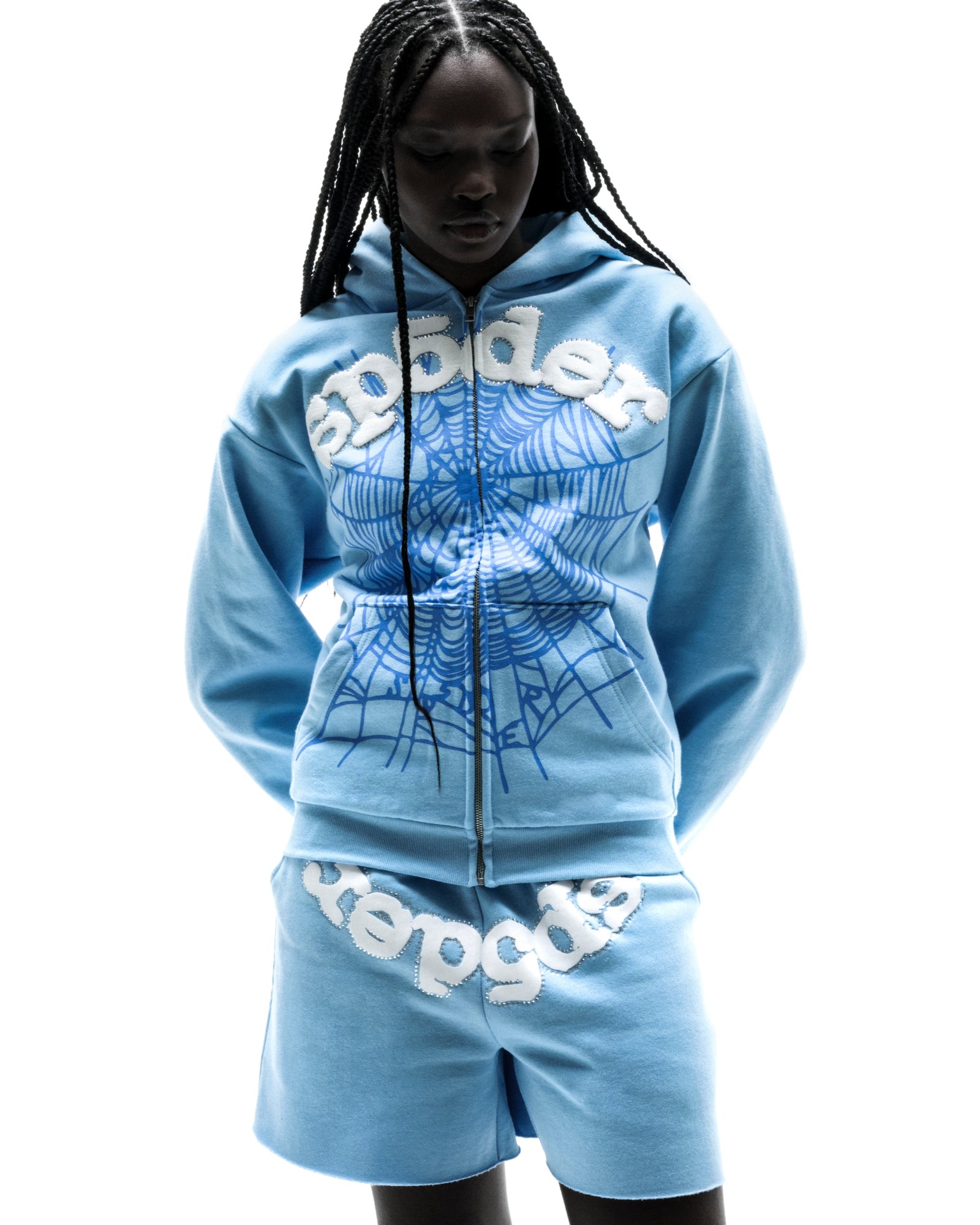 Model wearing a light blue OG WEB ZIP UP hoodie and matching shorts with white puff print lettering and a spiderweb graphic.