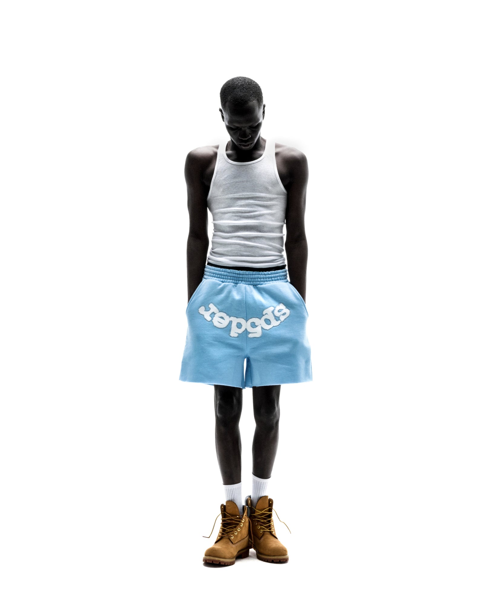 Model wears light blue OG WEB SWEATSHORT with white "SP5DER" text, raw hem, and drawcord waistband.