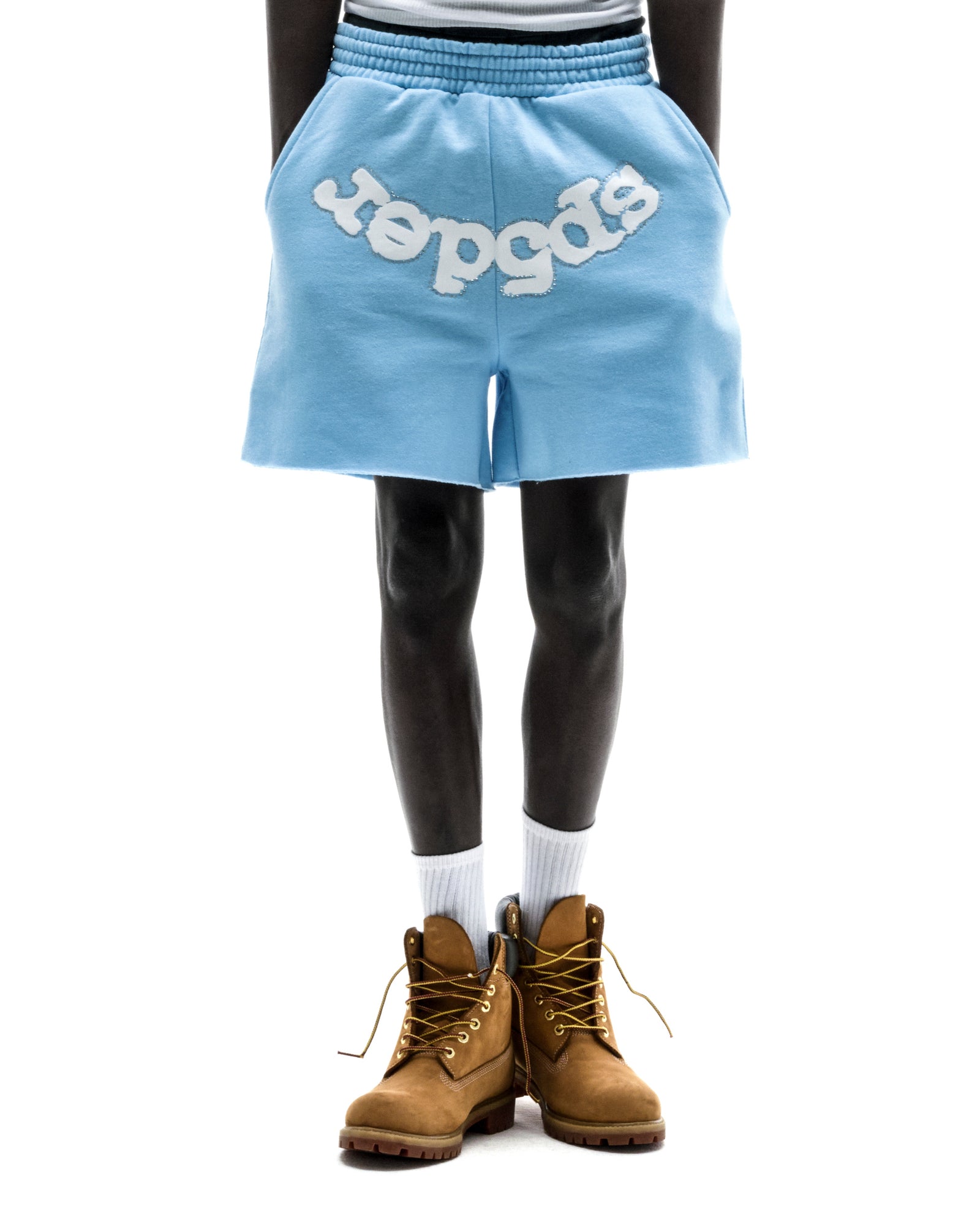 Model wearing light blue OG WEB SWEATSHORT with "SP5DER" text, raw hem, and drawcord waistband.