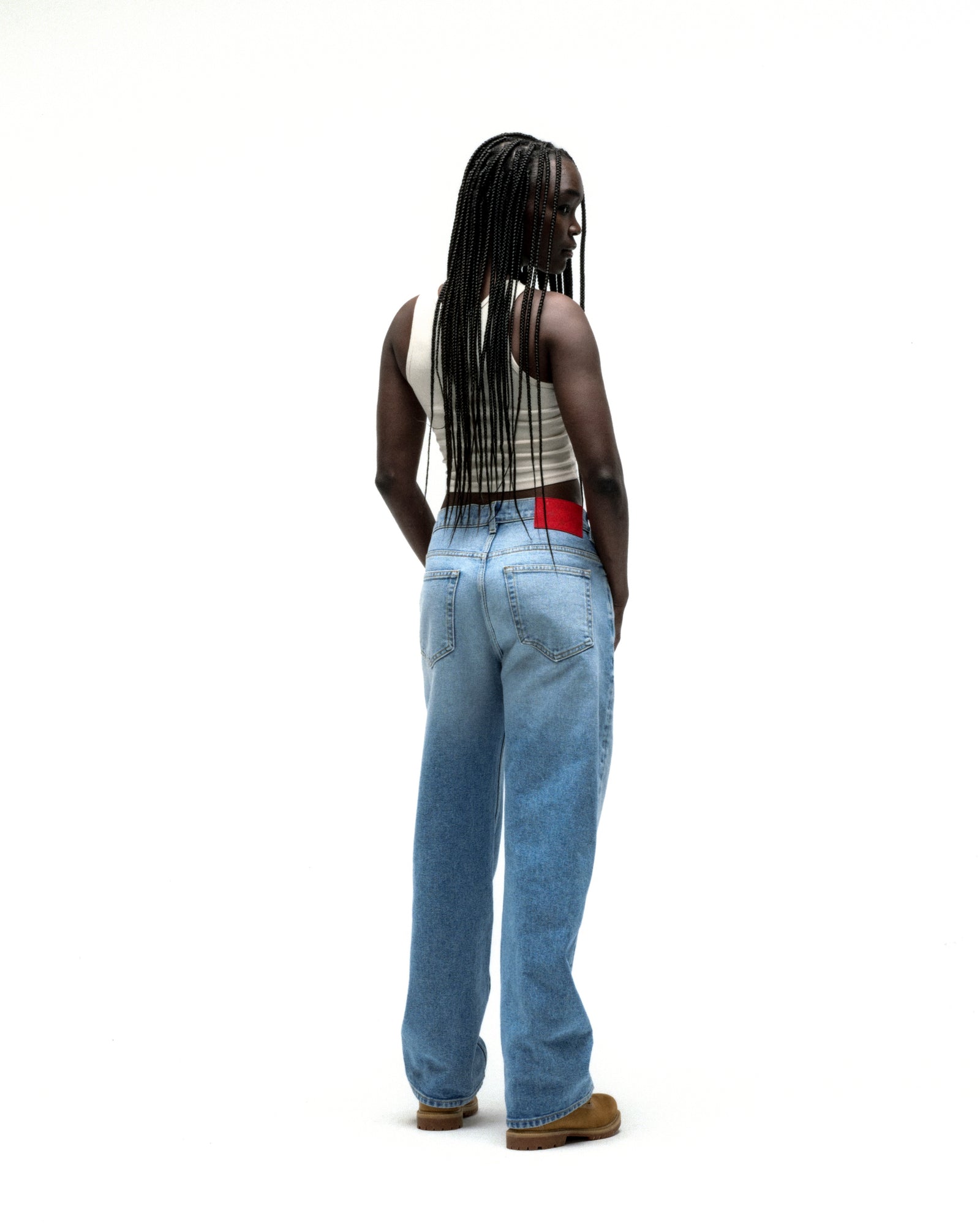 Model wearing vintage wash distressed logo denim jeans with a red back patch and straight leg fit.