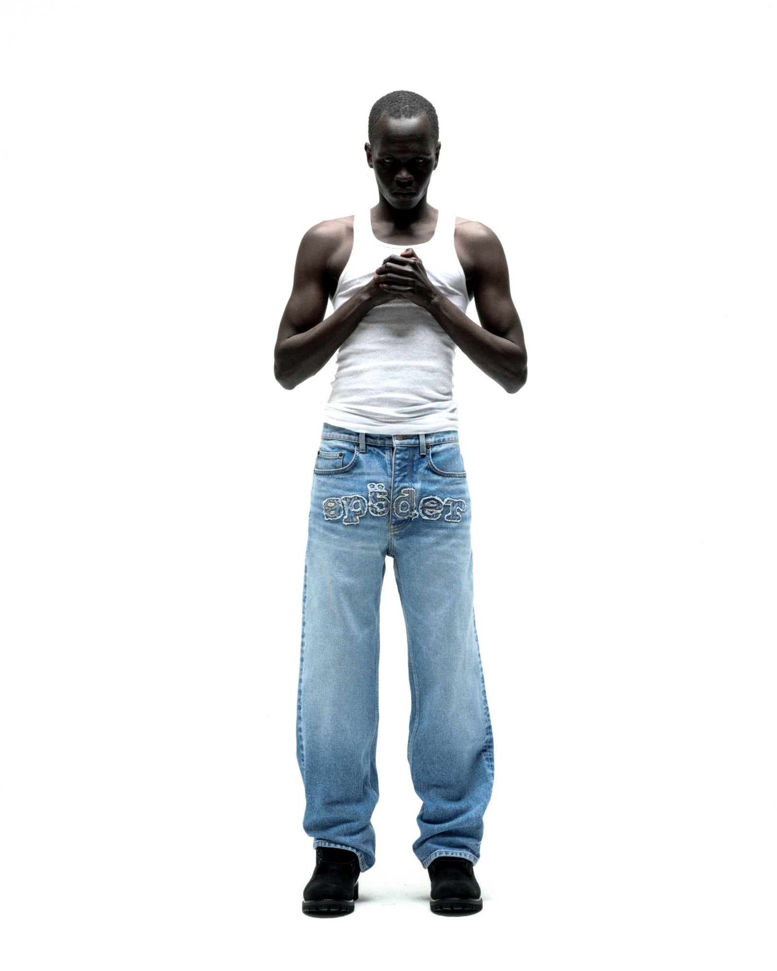 Man in vintage wash distressed logo V3 denim jeans with frayed "SP5DER" embroidery.
