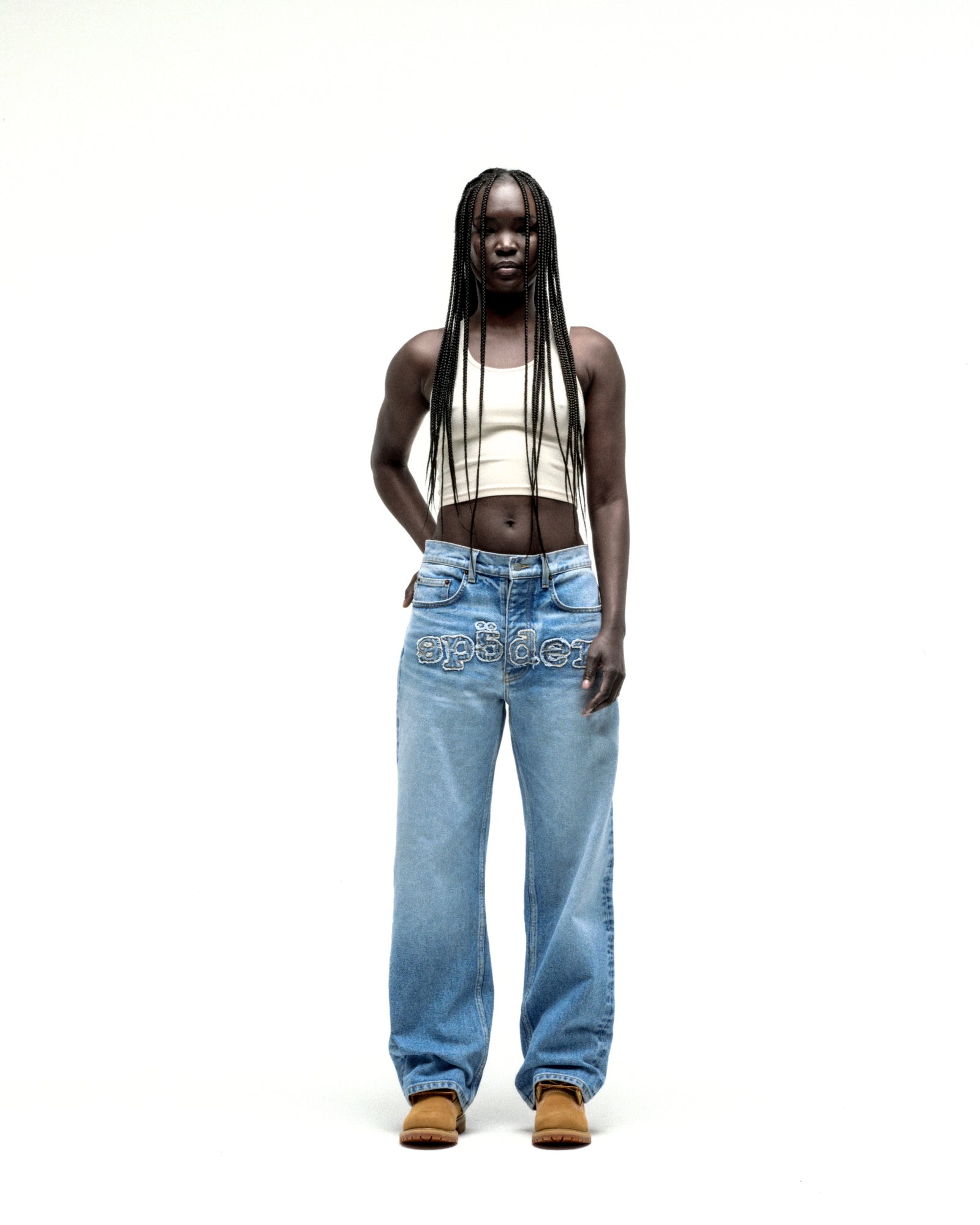 Model wearing vintage wash, straight leg denim jeans with frayed "SP5DER" logo across the crotch.