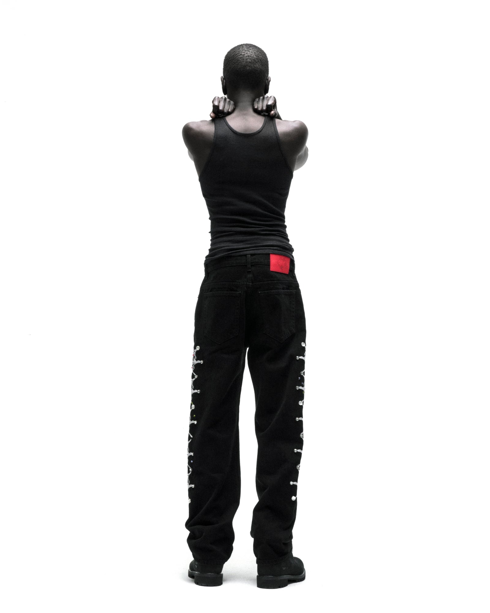 Black vintage wash denim pants with web print and rhinestone embellishments down both legs, worn by a person from behind.