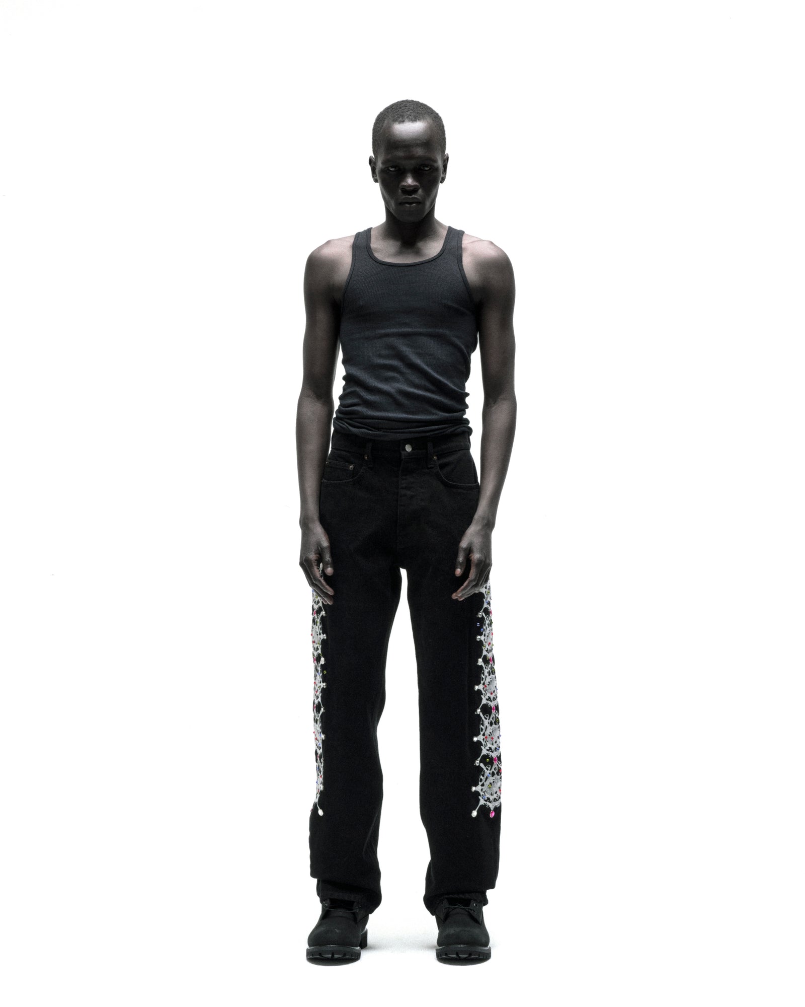 Man wearing vintage wash black denim pants with web print and rhinestone embellishments down both legs.