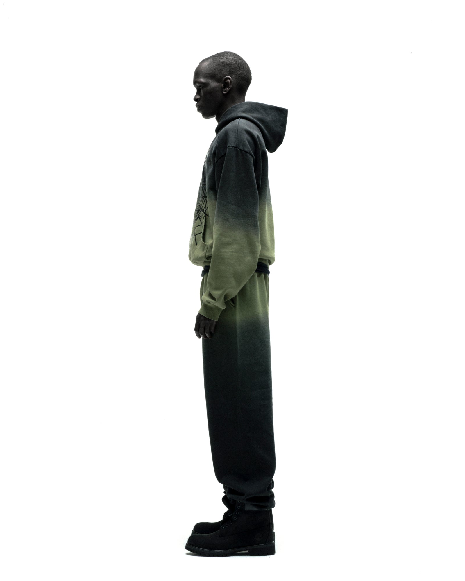 Man in OG Web Ombre Hoodie and sweatpants, fading from dark to light green, with a front graphic.