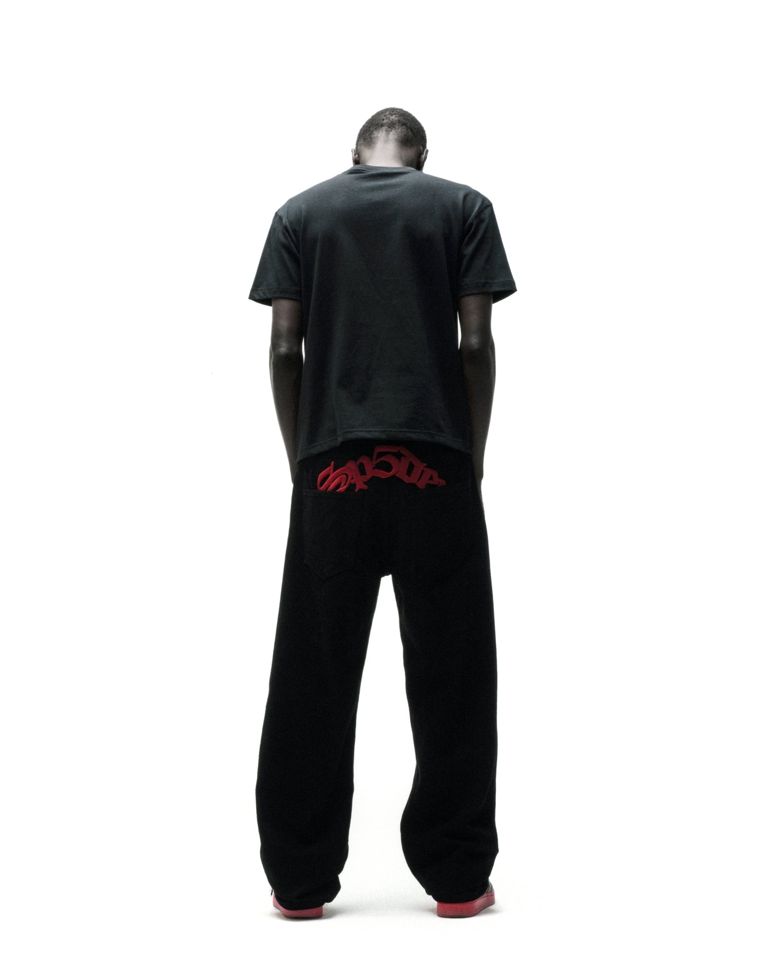 Man in black t-shirt and black pants with red "SP5DER" graphic on the back.