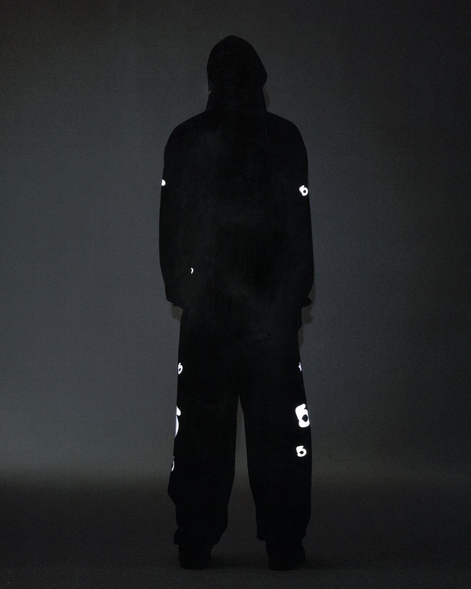 Dark figure wearing a black reflective Beluga hoodie and matching pants with 'SP5DER' and star prints.