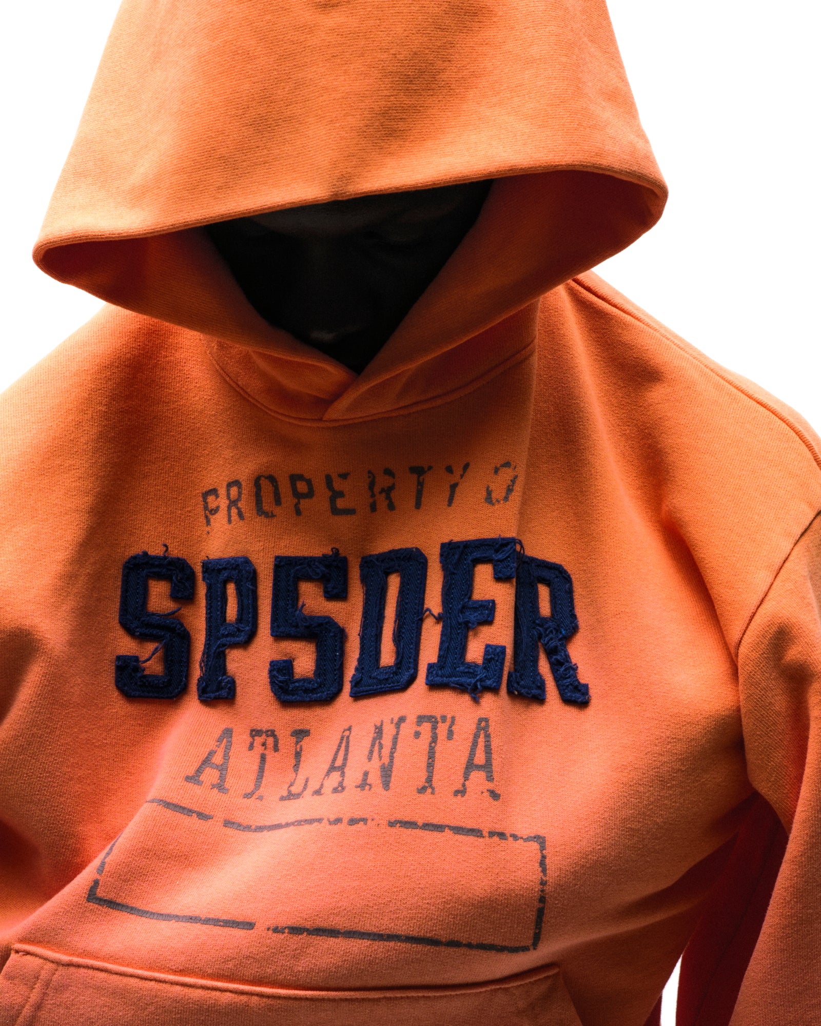Orange cotton fleece hoodie with raised, frayed "SPSDER" lettering and faded graphic print.