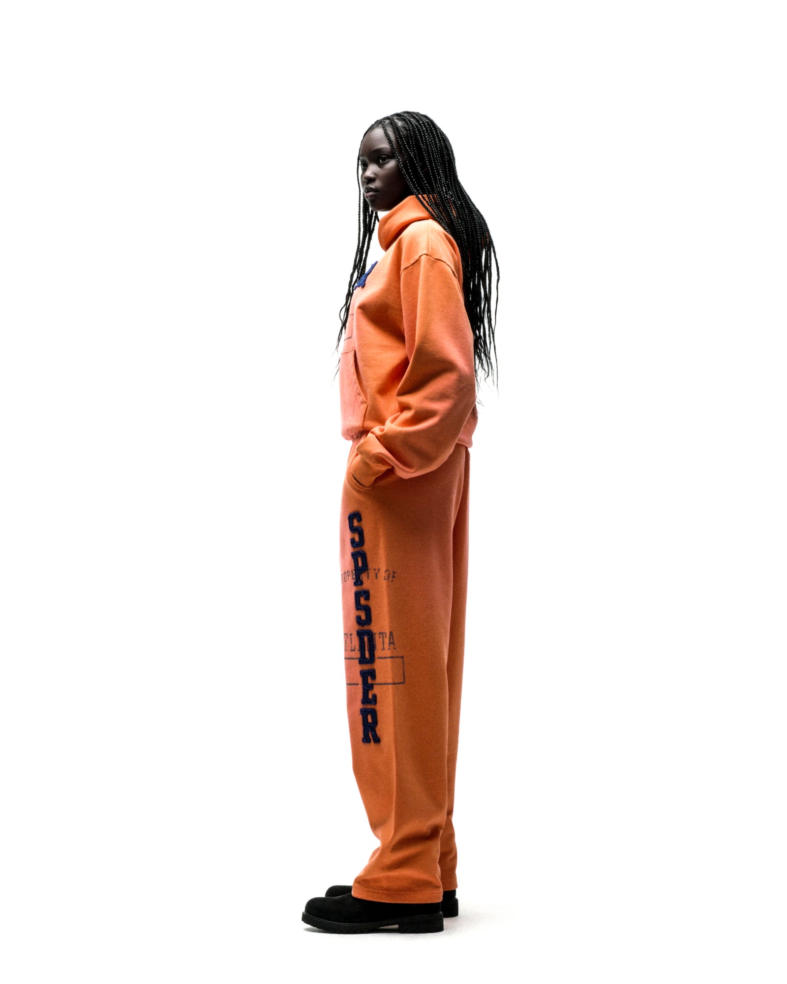 Model in an orange ISSUE 404 HOODIE and sweatpants with raised "SPSDER" lettering.