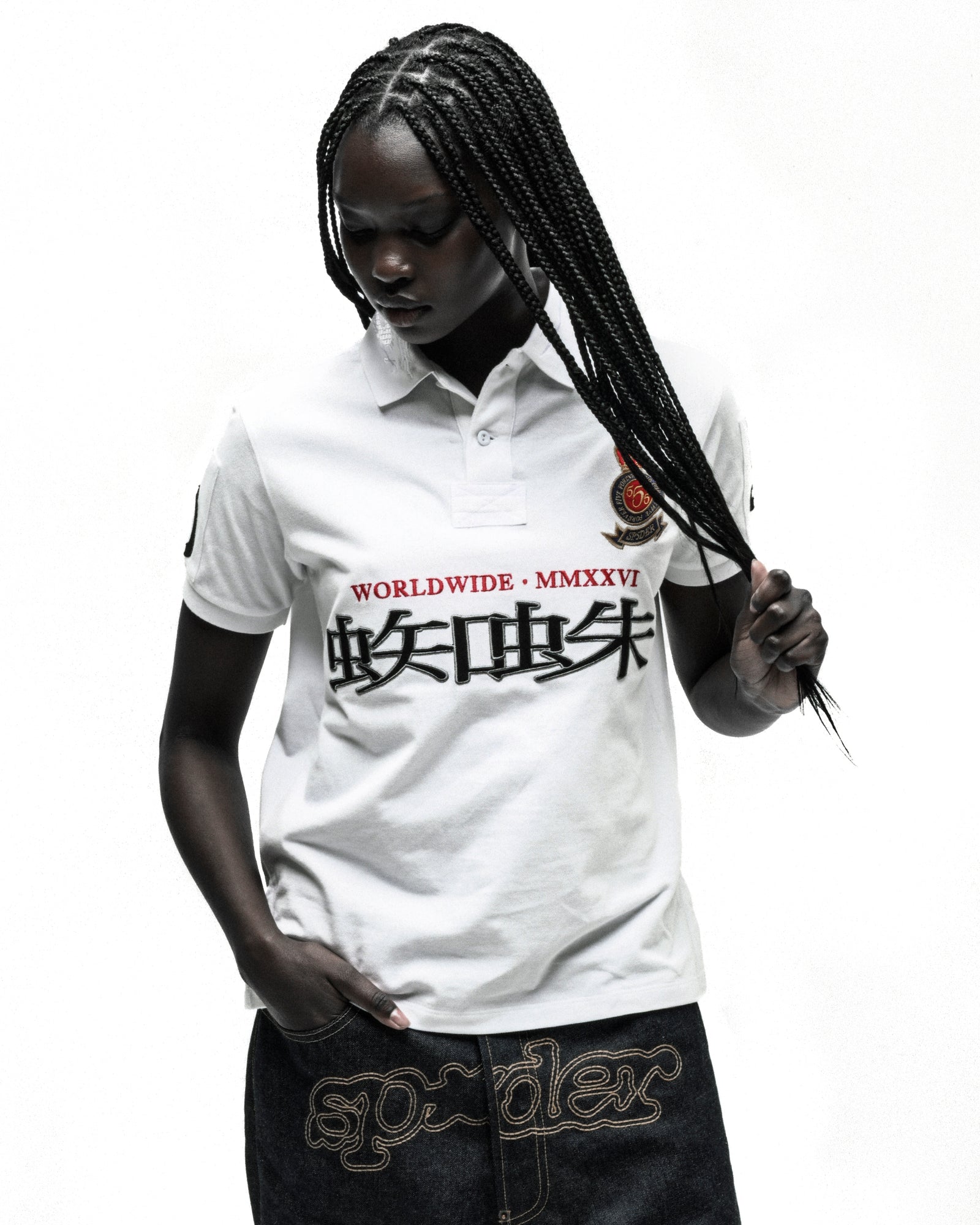 Woman in white "WORLDWIDE MMXXVI" polo shirt with black Japanese text and embroidered crest, dark denim shorts.