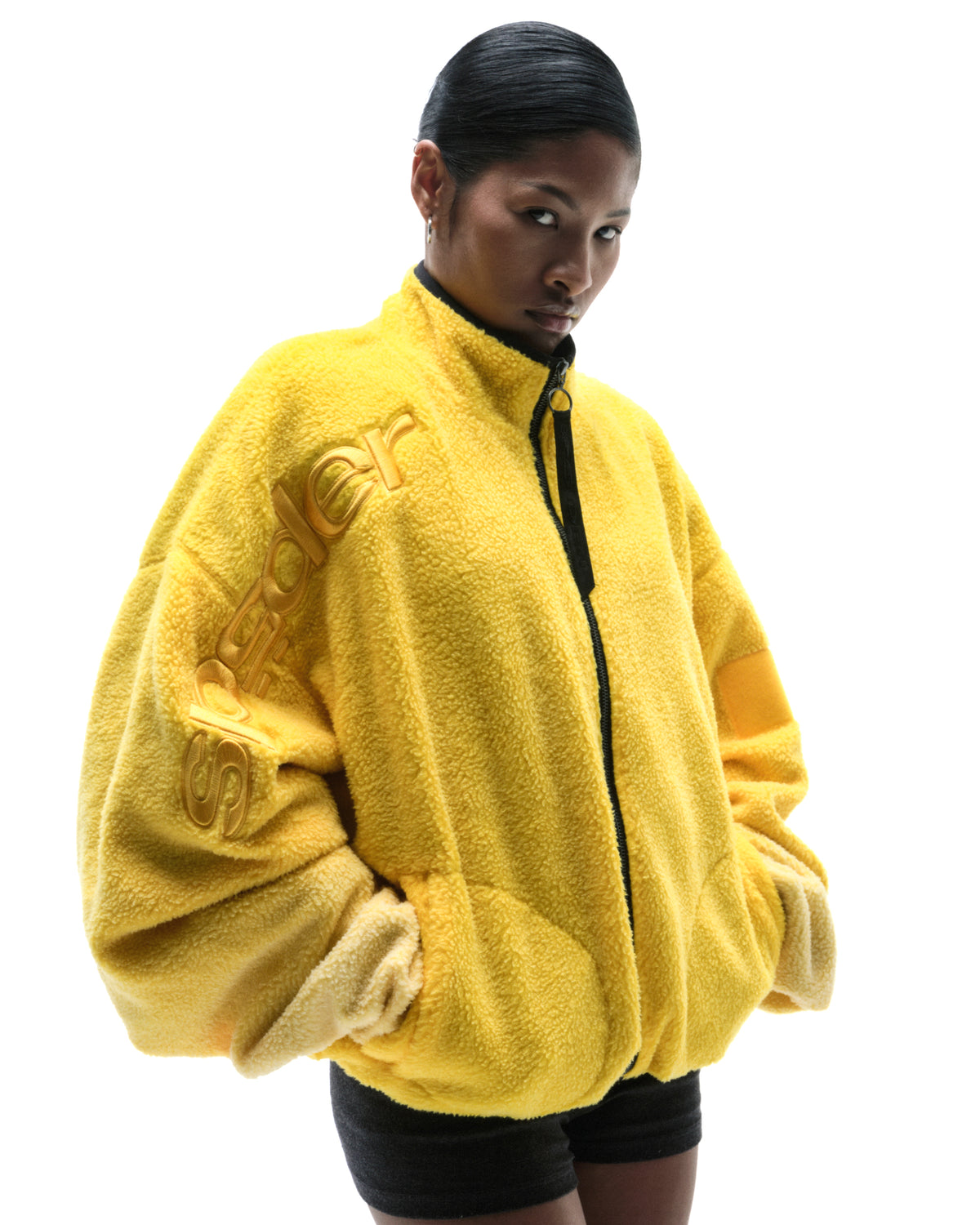 Model wearing a bright yellow, oversized fleece zip-up jacket with embossed Spyder branding on the sleeve.