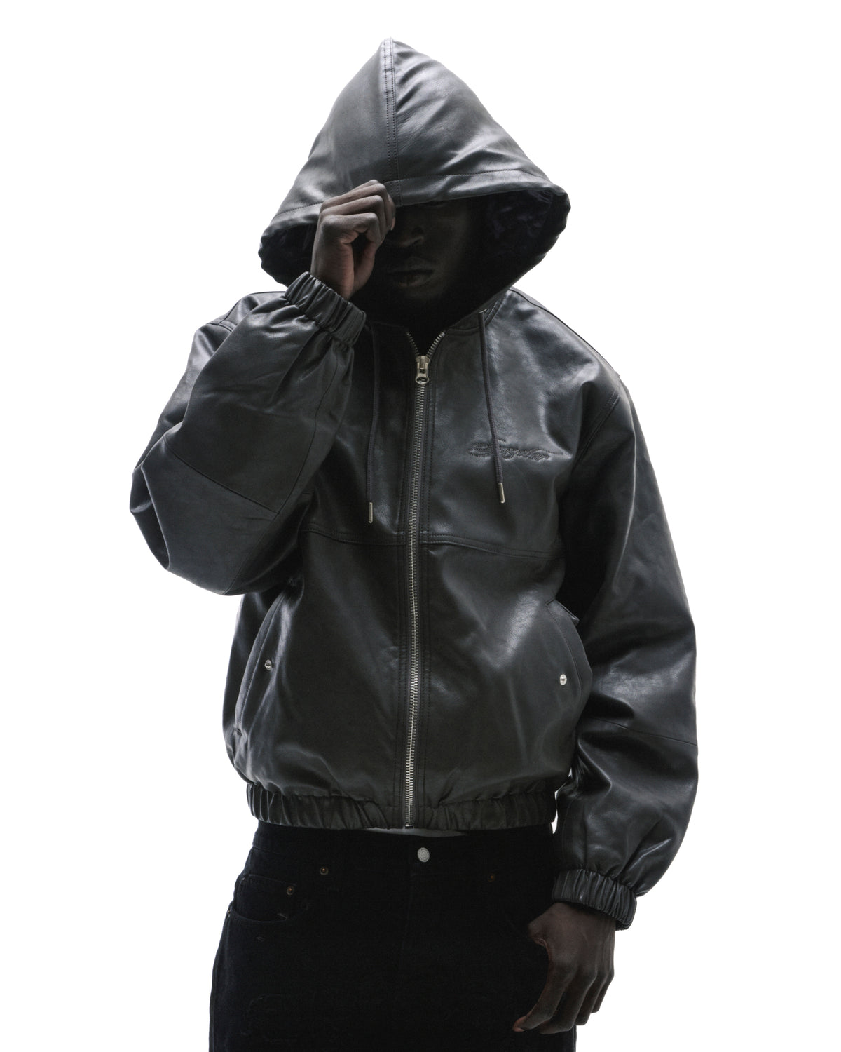 Model wearing a black leather zip-up hoodie with a drawstring hood and elastic cuffs against a white background.