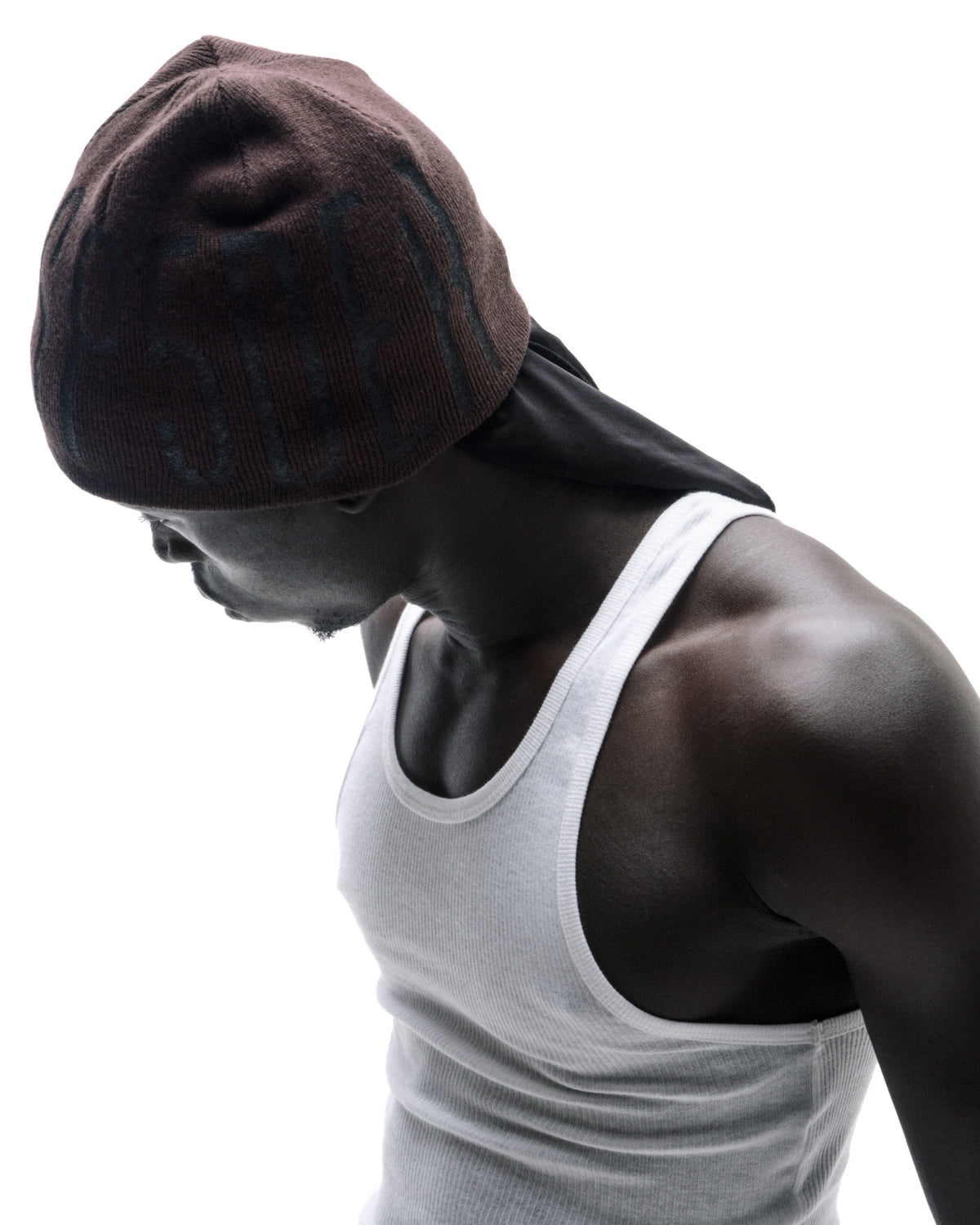Model wearing a brown beanie over a black durag and a white ribbed tank top against a white background.
