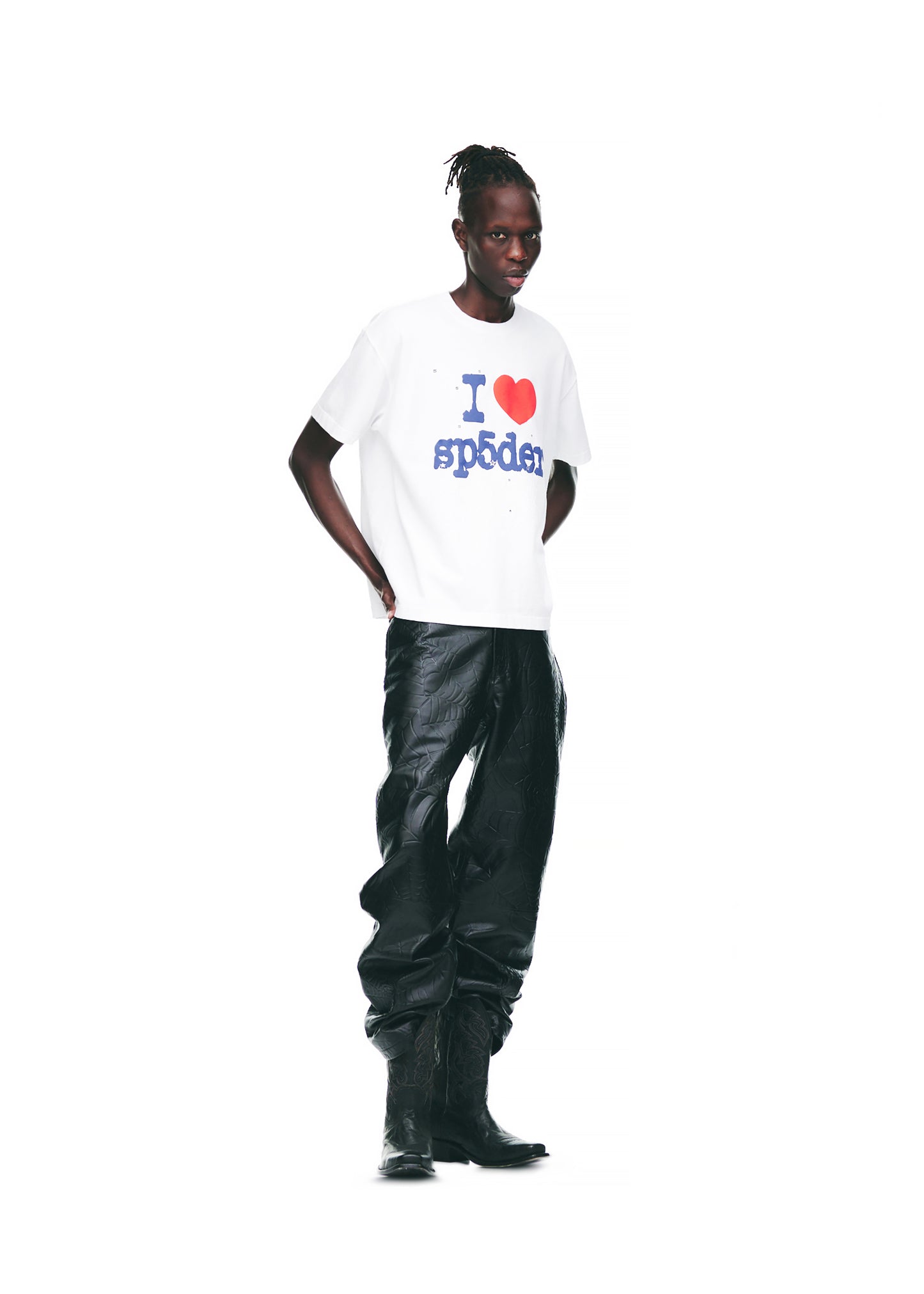Male model in white cotton Souvenir Tee with "I ❤️ sp5der" graphic, black textured pants, and boots.
