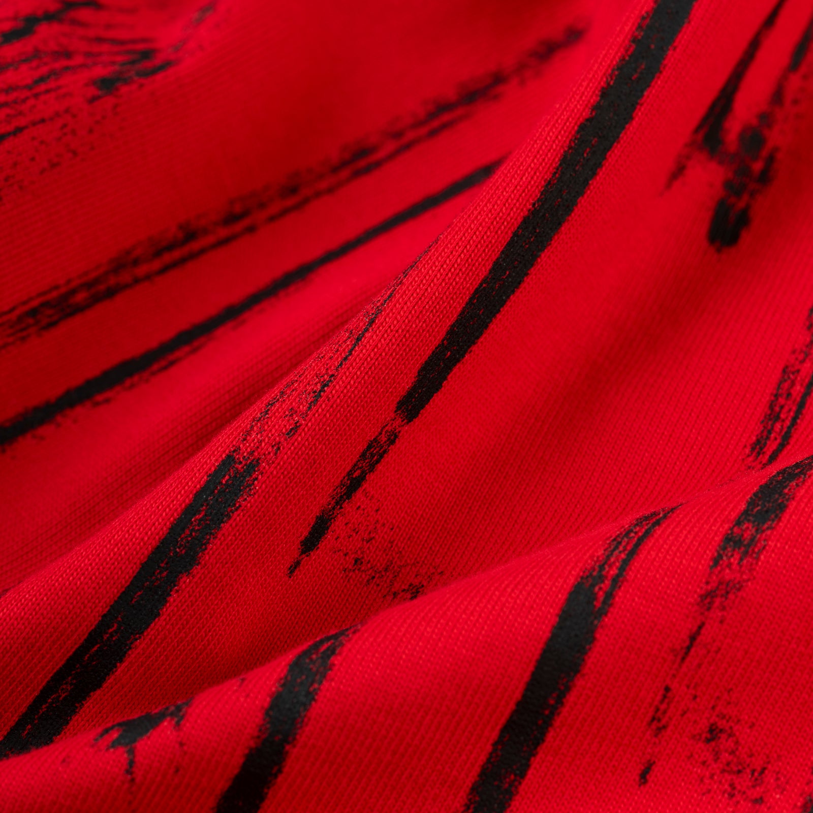 Close-up of a red 100% cotton tee with black distressed brushstroke graphic print.
