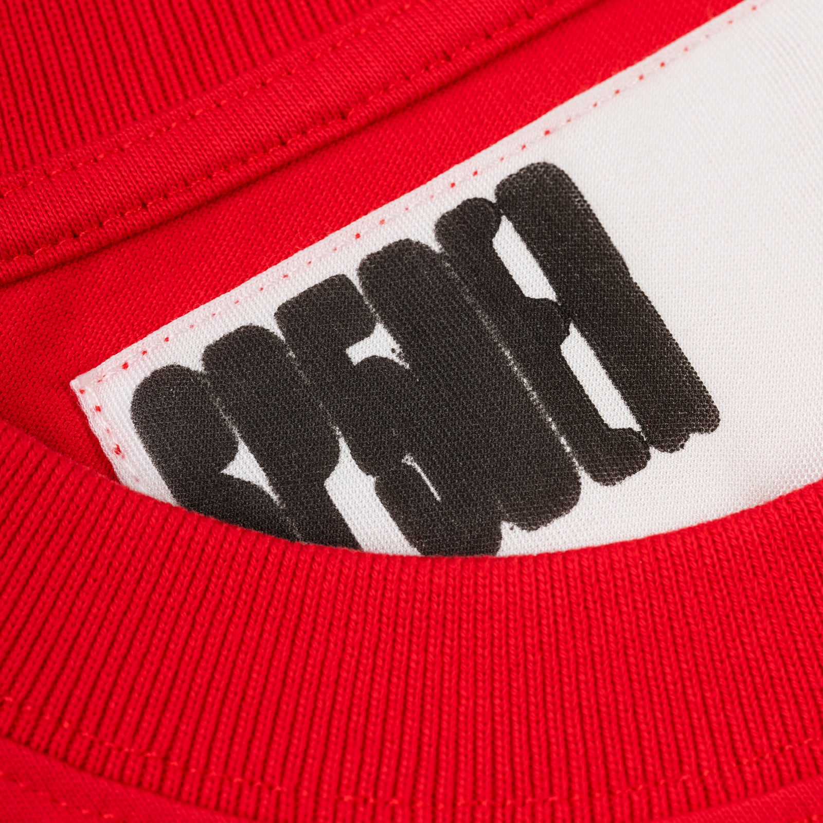 Close-up of a red cotton tee with a white neck tag featuring the black 'SP5DER' logo.