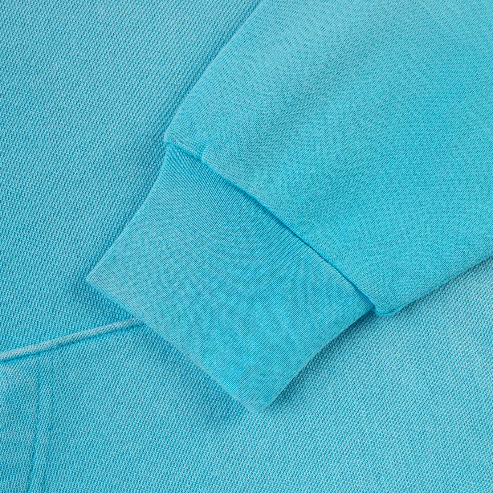 Close-up of a bright blue 13oz cotton fleece hoodie sleeve with rib knit cuff.