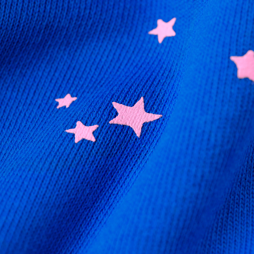 Close-up of blue cotton fleece sweatpants with scattered pink star puff prints.