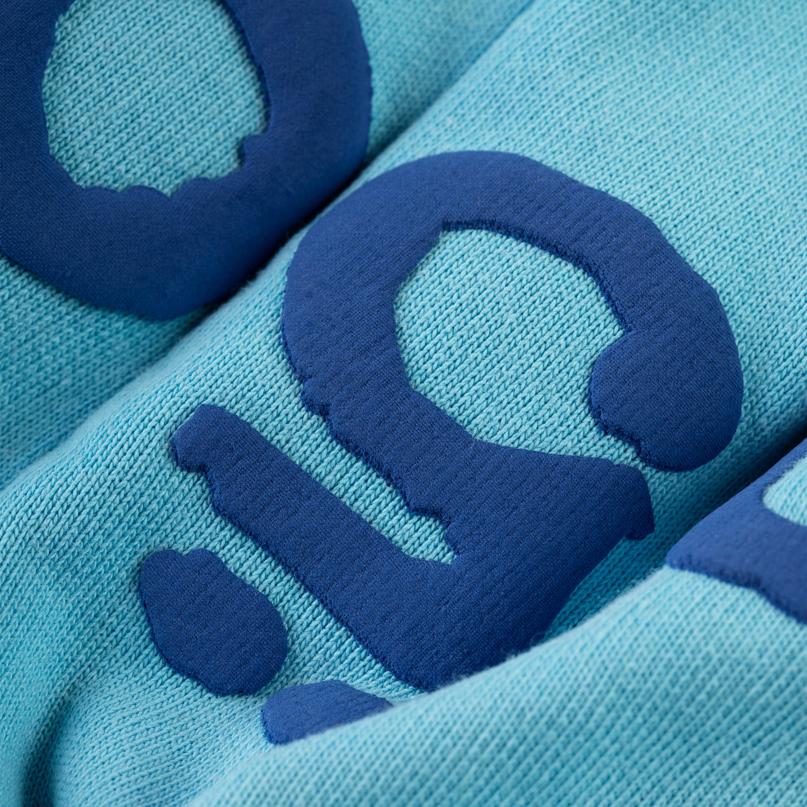 Close-up of light blue cotton fleece sweatpant with dark blue puff print lettering.