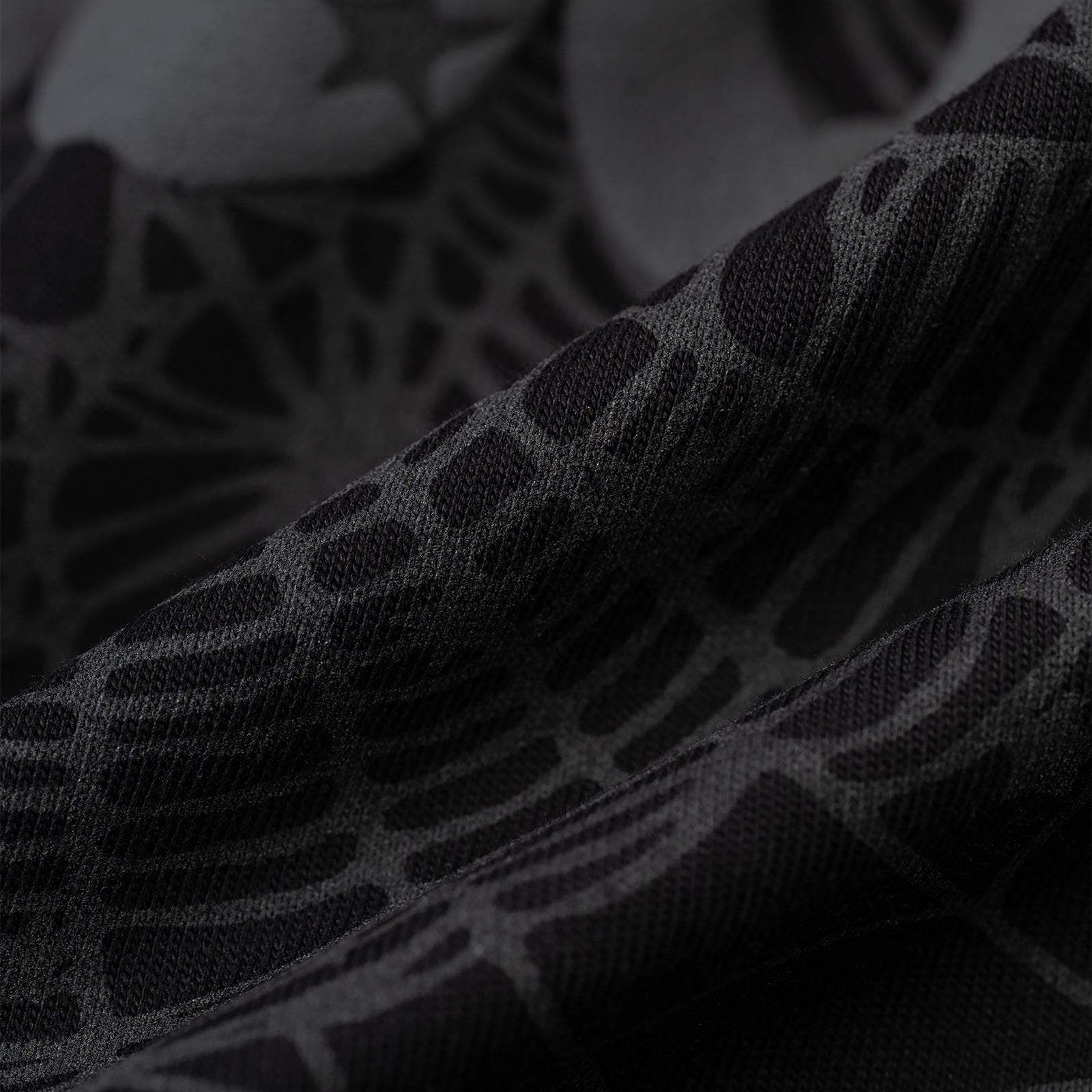 Close-up of black Phantom Souvenir Baby Tee fabric with subtle dark gray web-like pattern.