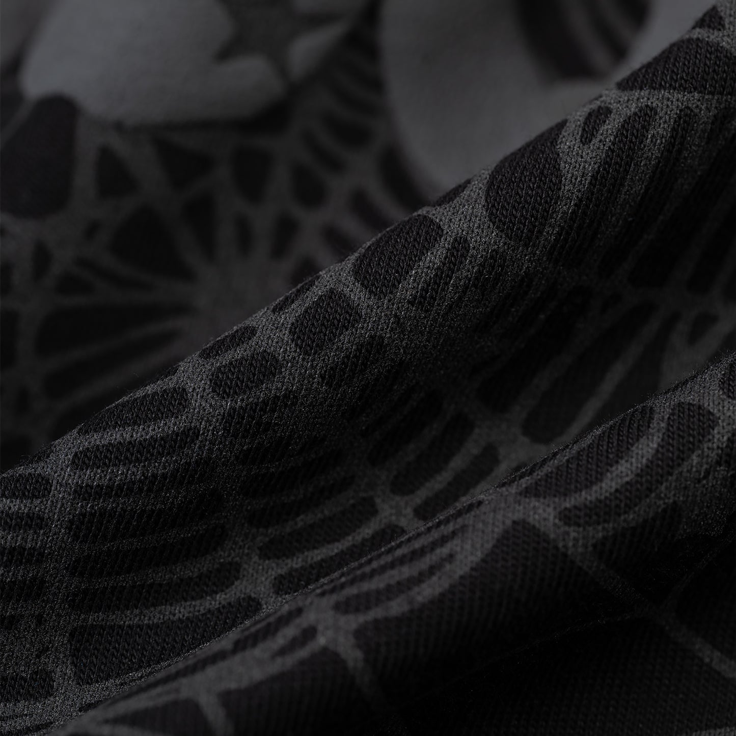 Close-up of black Phantom Souvenir Men's Tee fabric with subtle dark grey web and star pattern.