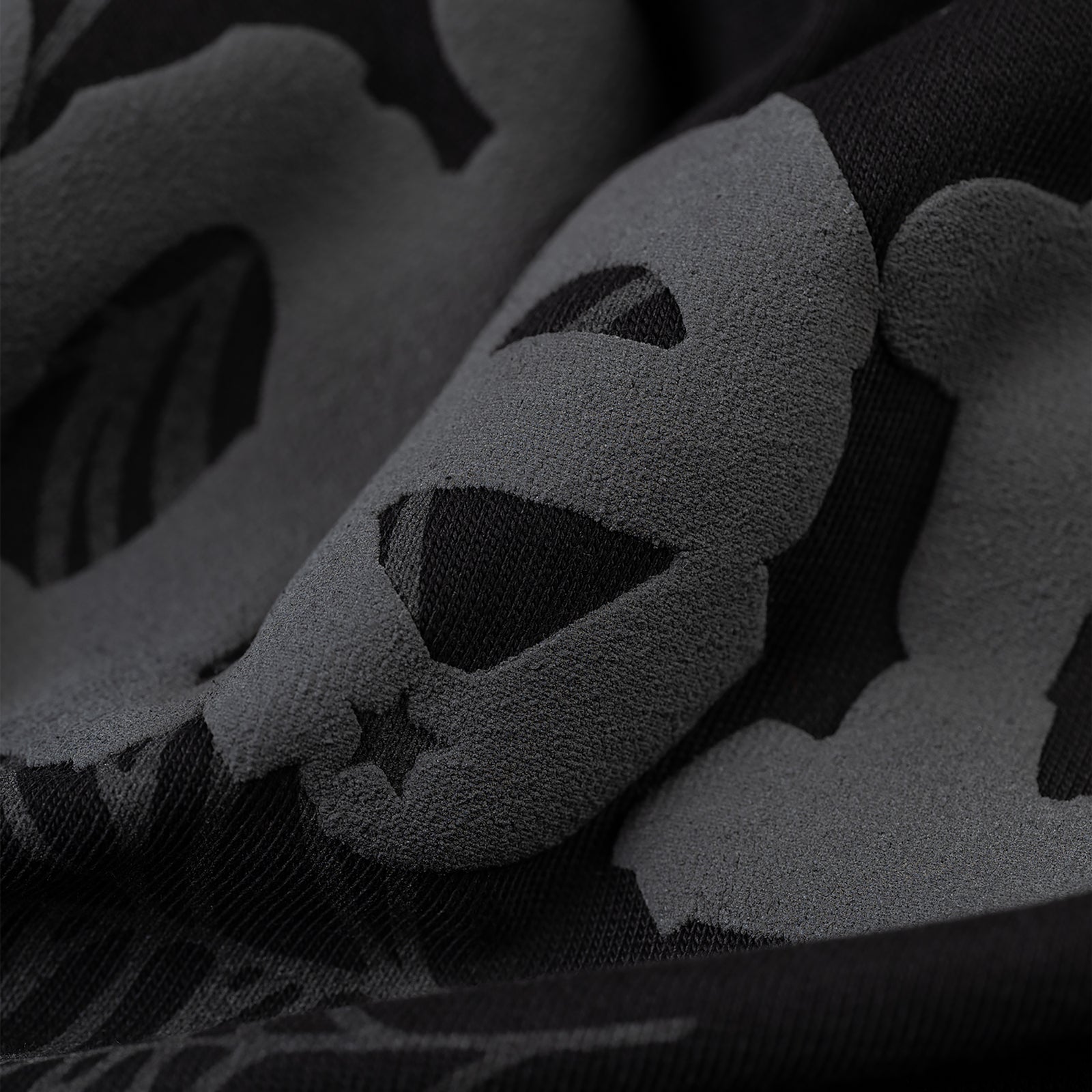 Close-up of black Phantom Souvenir Baby Tee fabric with dark grey skull and star pattern.