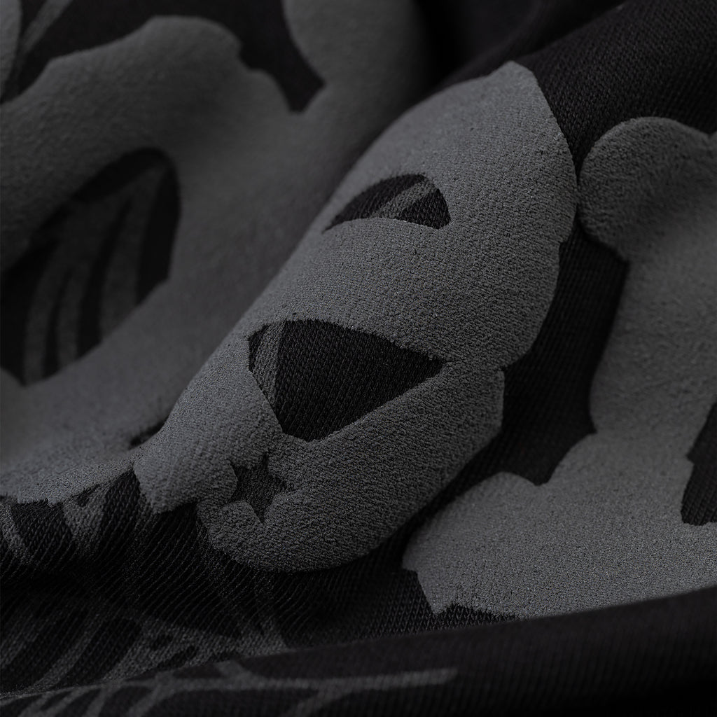 Close-up of black Phantom Souvenir Baby Tee fabric with dark grey skull and star pattern.