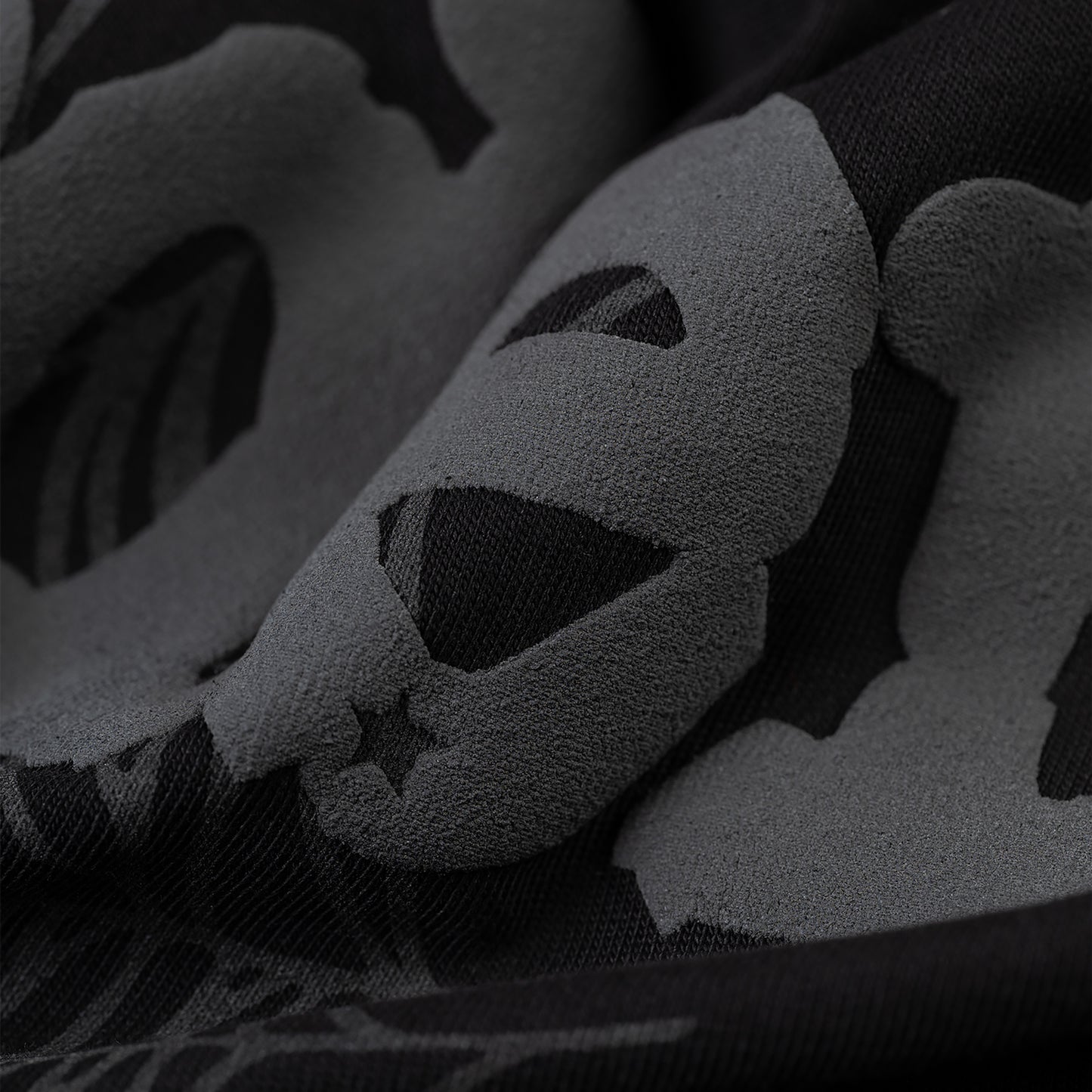 Close-up of a black men's tee with a subtle, dark gray Phantom skull and star pattern.