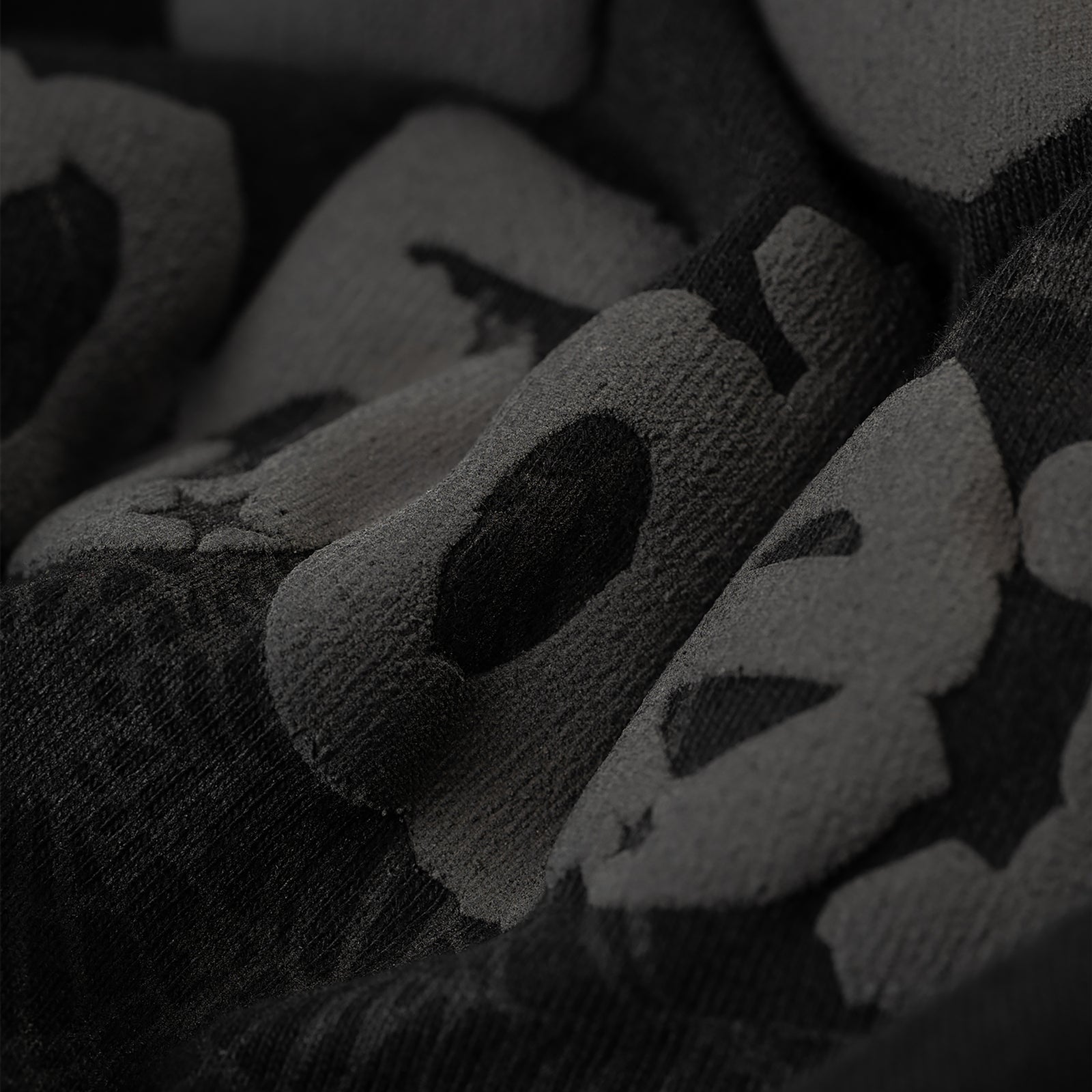 Close-up of a black Phantom Souvenir Baby Tee with subtle dark gray textured lettering.