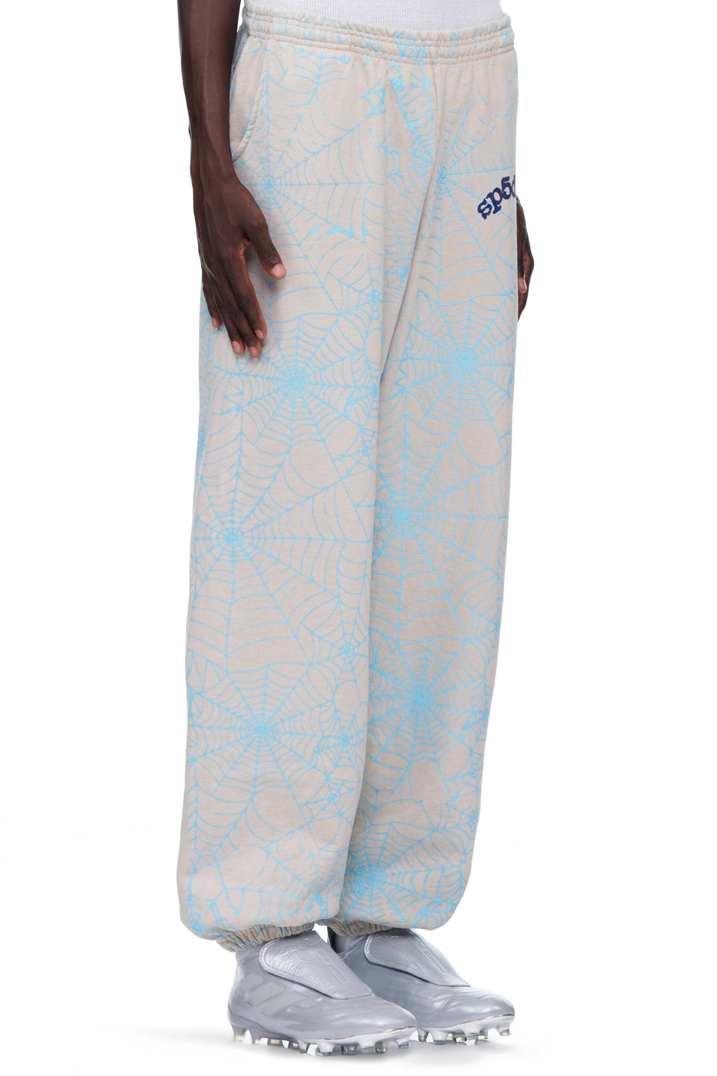 Beige 23oz fleece sweatpants with light blue cracked web print and "SP5DER" text on the upper leg.