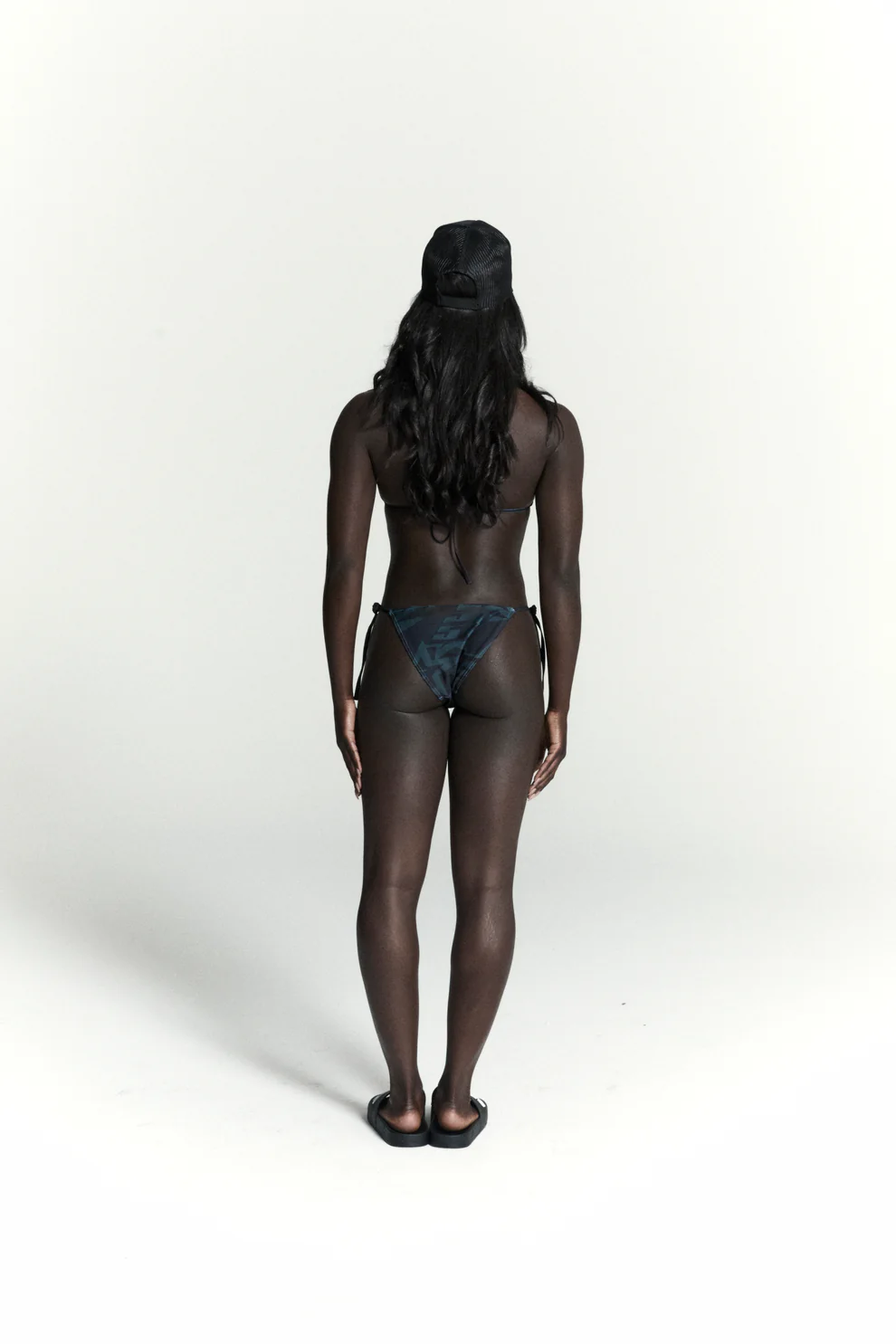 Woman from behind wearing a 5-star print bikini with rope ties and a black cap.