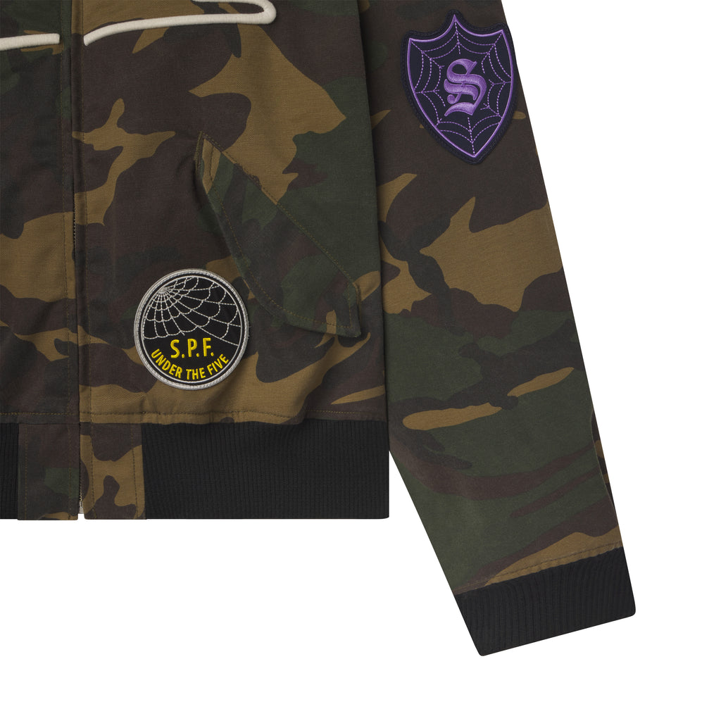 Camo print cotton canvas bomber jacket featuring graphic patches, flap pockets, and black rib-knit hem and cuffs.