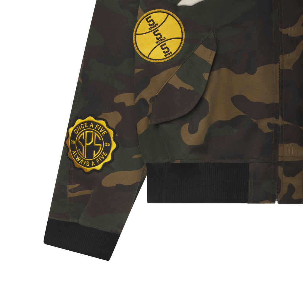 Camo cotton canvas bomber jacket featuring yellow circular graphic patches, flap pockets, and black rib-knit cuffs.