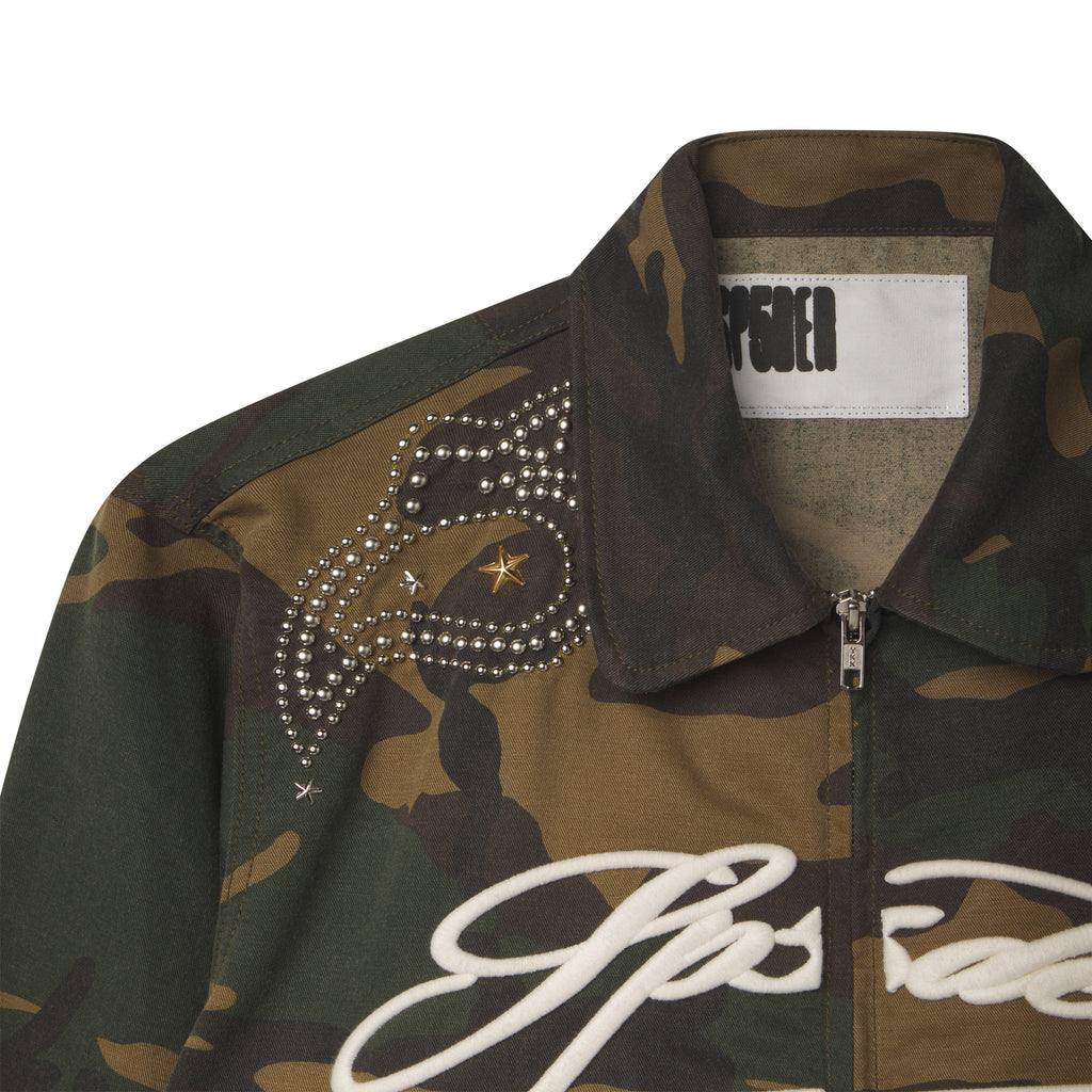 Camo cotton canvas bomber jacket with silver studded shoulder detailing, a spread collar, and white embroidered script text.