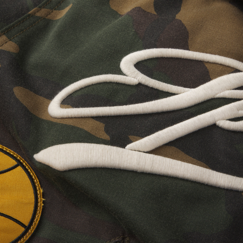 Cotton canvas camo bomber jacket featuring white embroidered script text and a circular yellow graphic patch.
