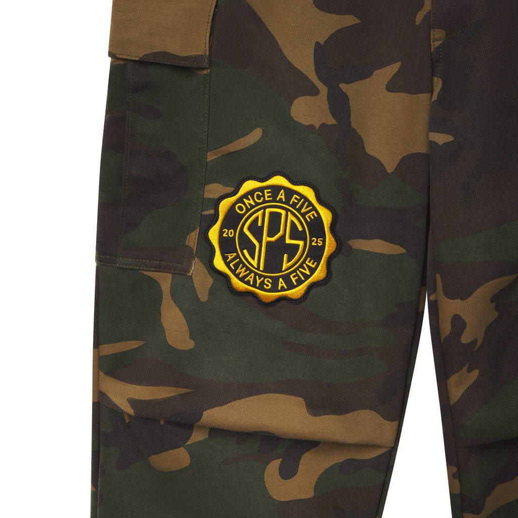 Cotton canvas camo cargo pants featuring a yellow circular embroidered graphic patch with SPS branding and side cargo pockets.