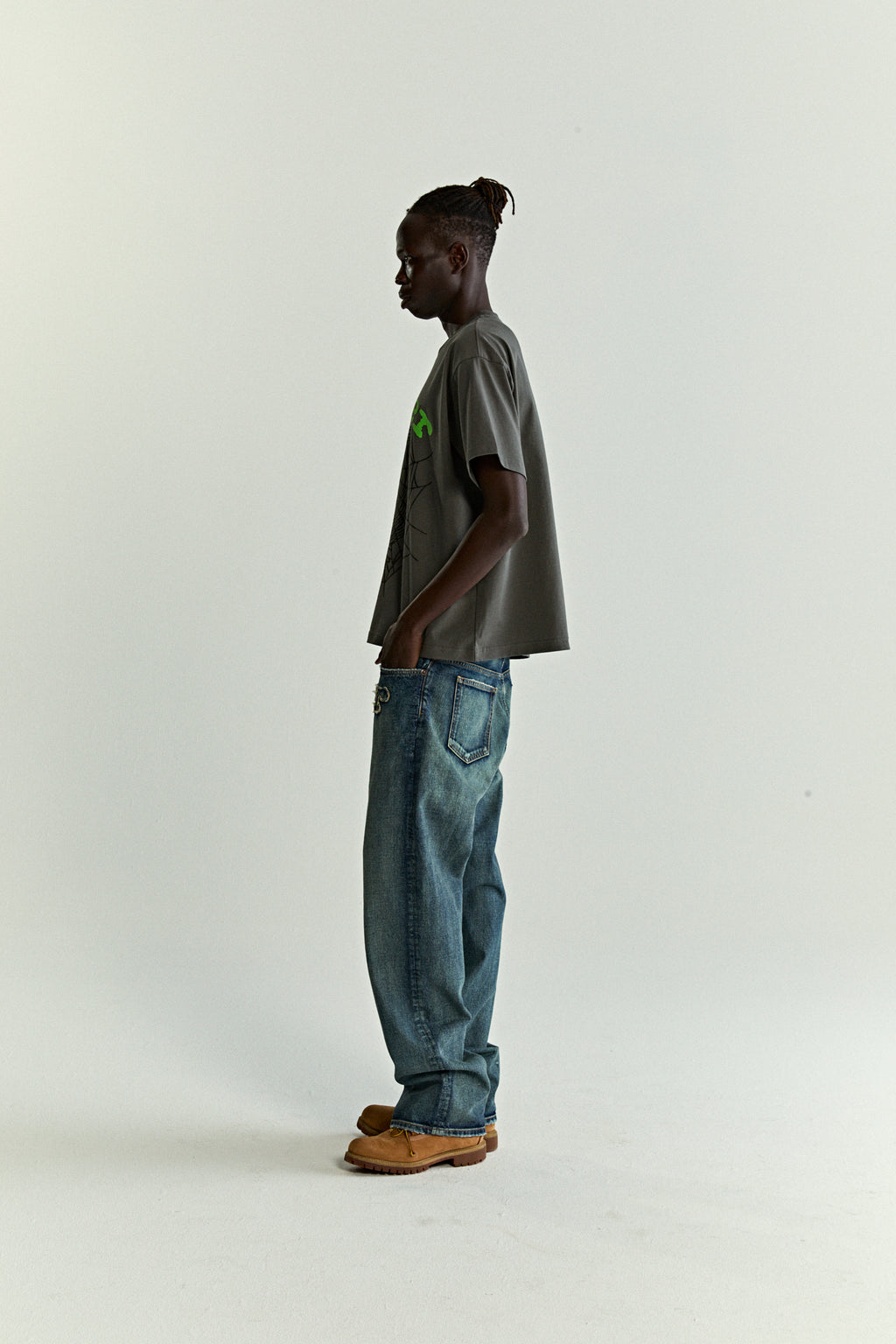 Model in standard fit gray OG WEB V2 TEE with green puff/discharge print, blue jeans, and brown shoes.