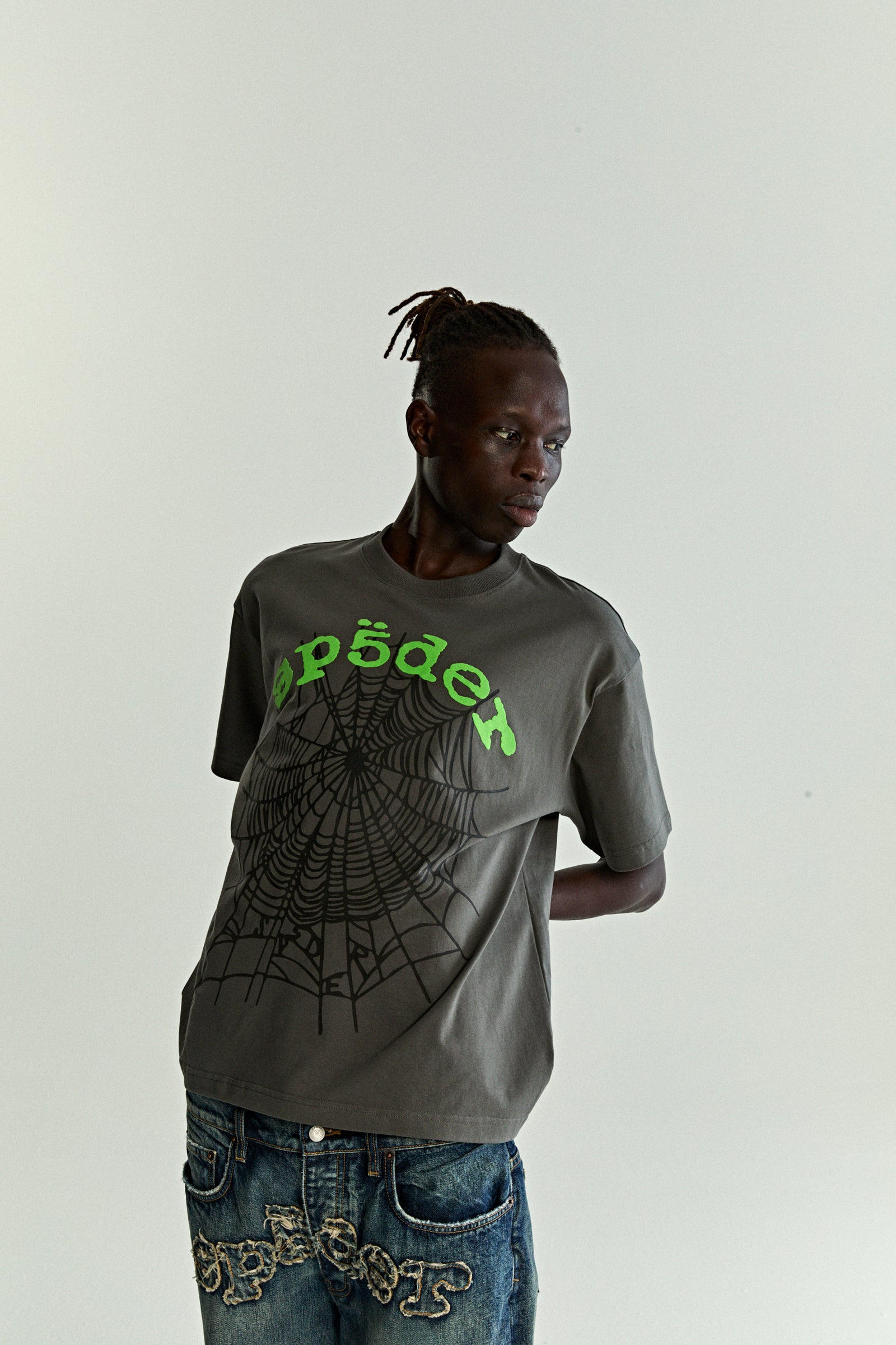 Man in a gray cotton OG WEB V2 TEE with green puff print text and a black spiderweb graphic.