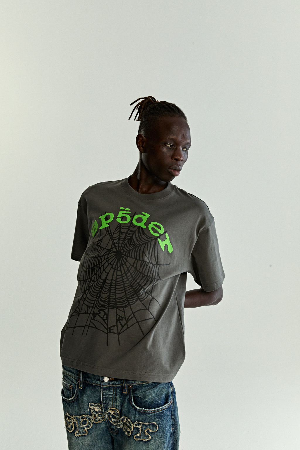 Man in a gray cotton OG WEB V2 TEE with green puff print text and a black spiderweb graphic.