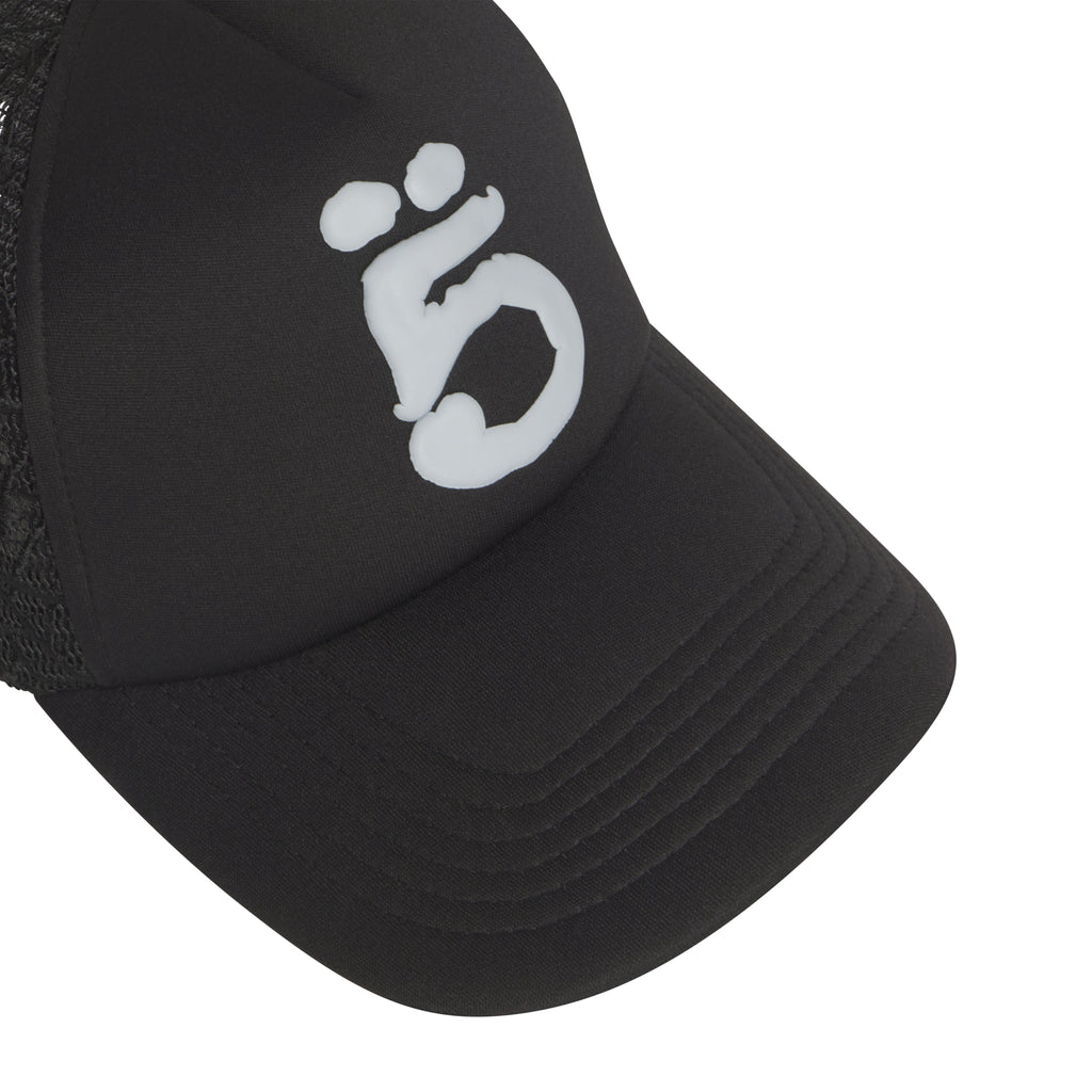 Black trucker hat with a white puff print graphic logo, curved brim, and breathable mesh side panels.
