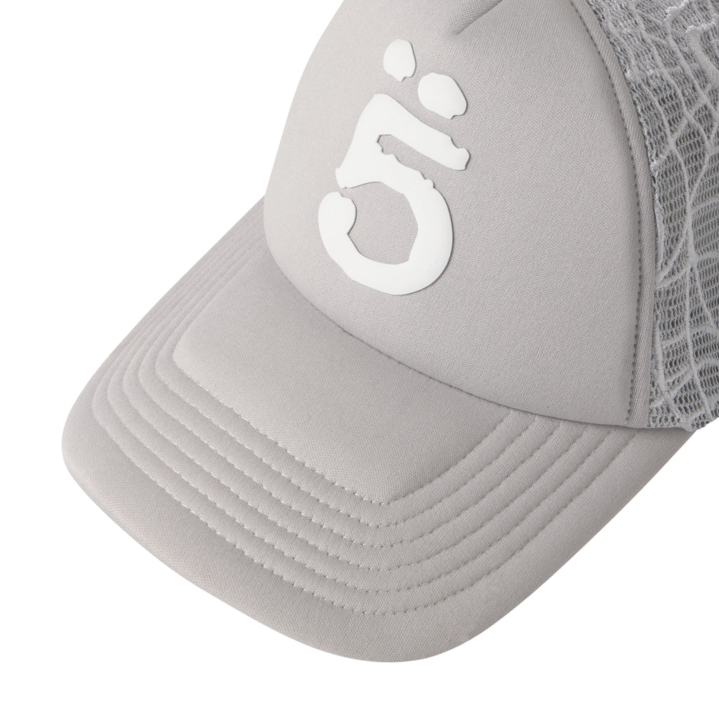 Grey trucker hat with a white puff print logo, curved brim, and detailed embroidered web mesh side panels.