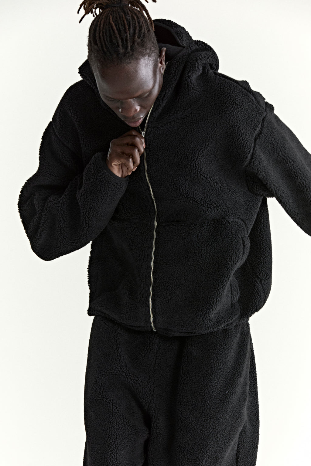 Black teddy fleece zip-up hooded jacket with welt pockets, worn by a person zipping it up.