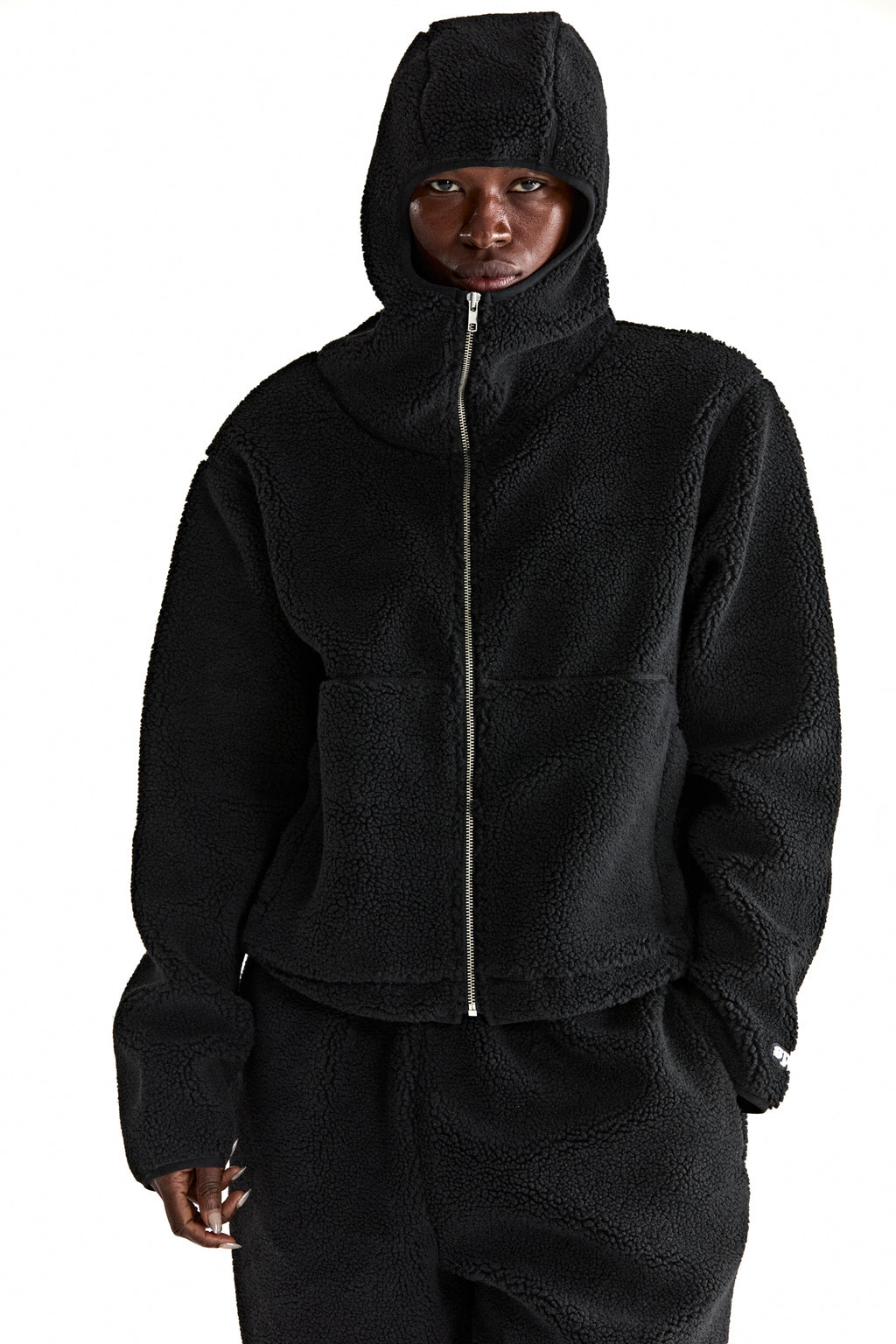 Black teddy fleece zip-up hooded jacket with rubberized logo patch and welt pockets.