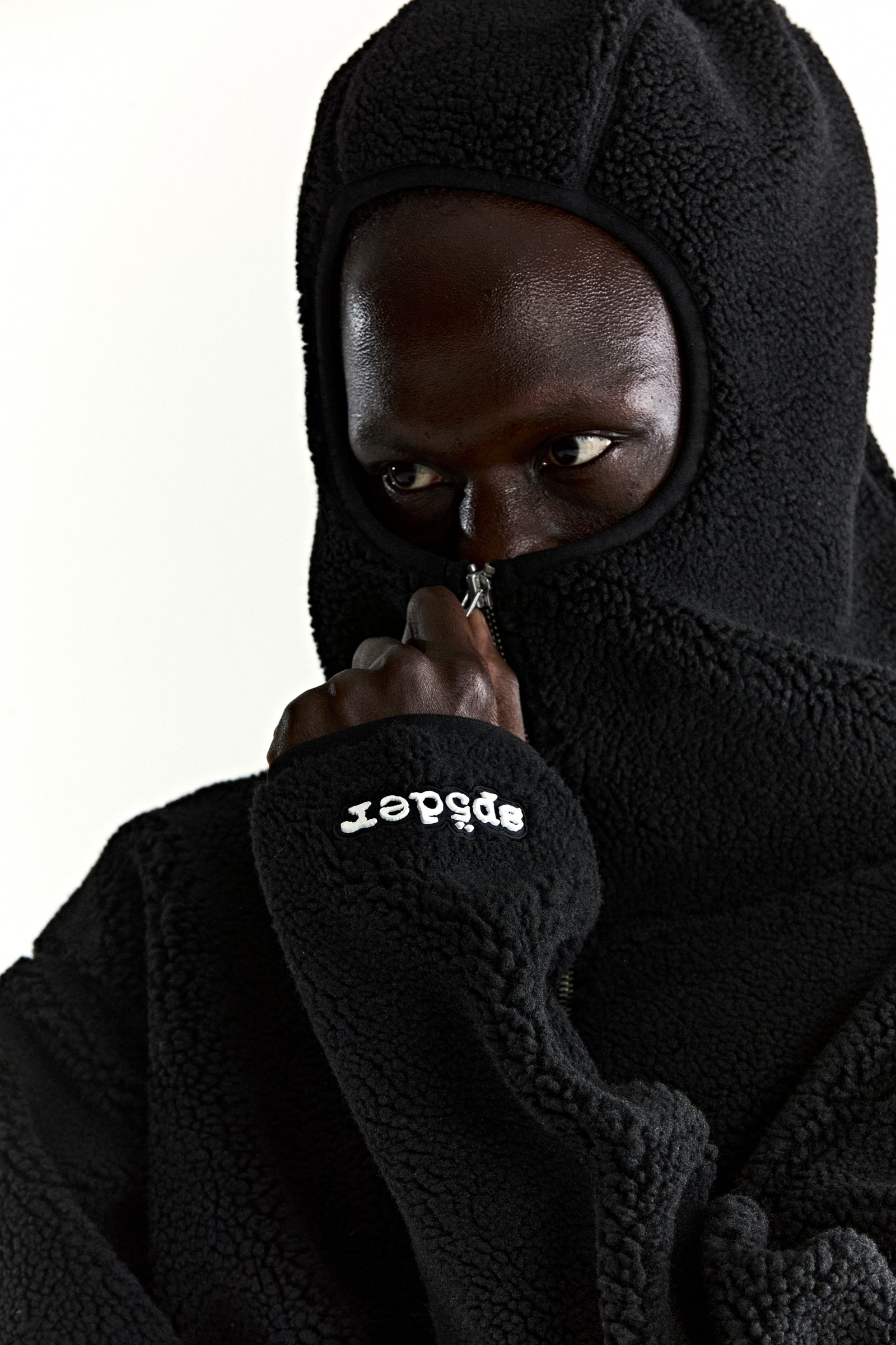 Black teddy fleece zip-up jacket with hood, featuring a rubberized "sp5der" logo patch on the wrist.