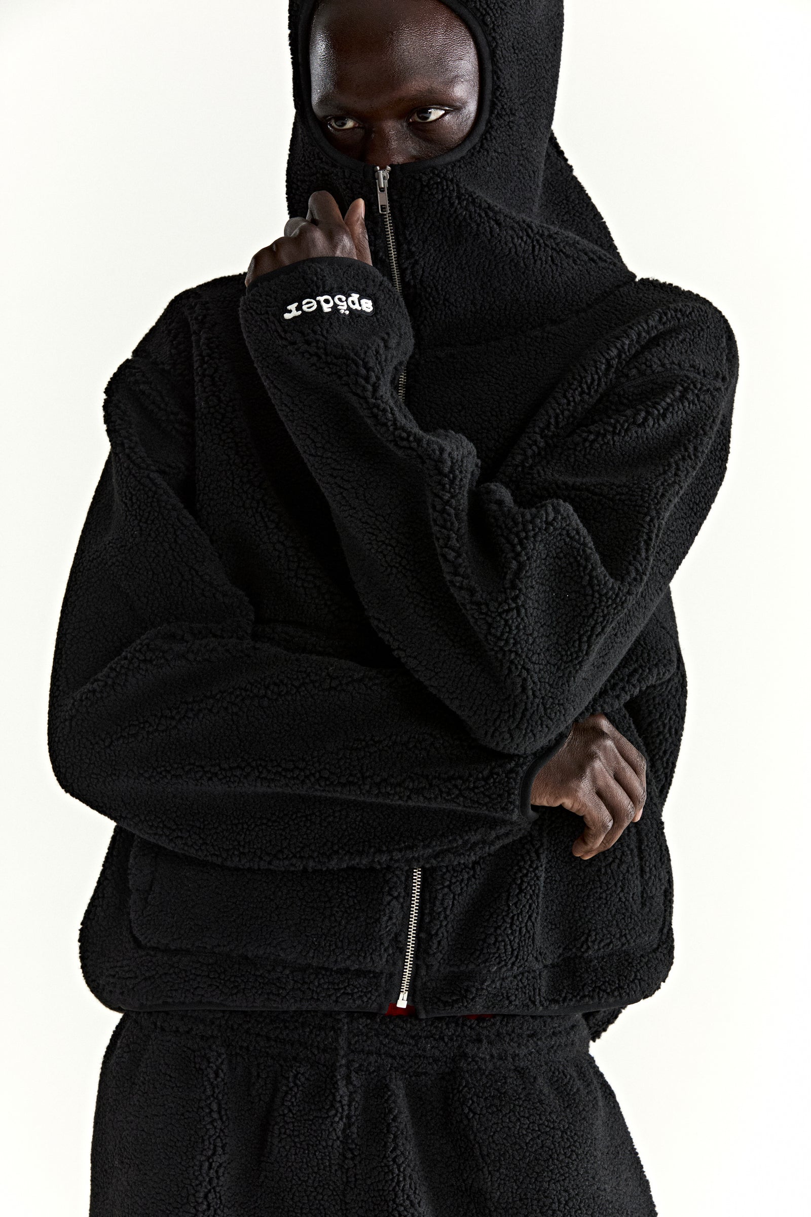 Black teddy fleece zip-up jacket with hood, rubberized logo on wrist, and welt pockets.