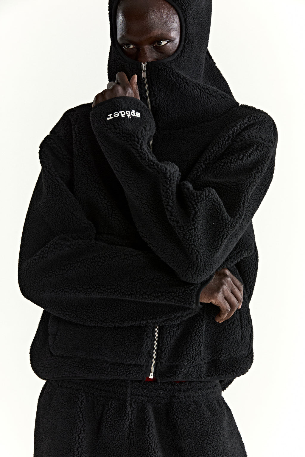 Black teddy fleece zip-up jacket with hood, rubberized logo on wrist, and welt pockets.