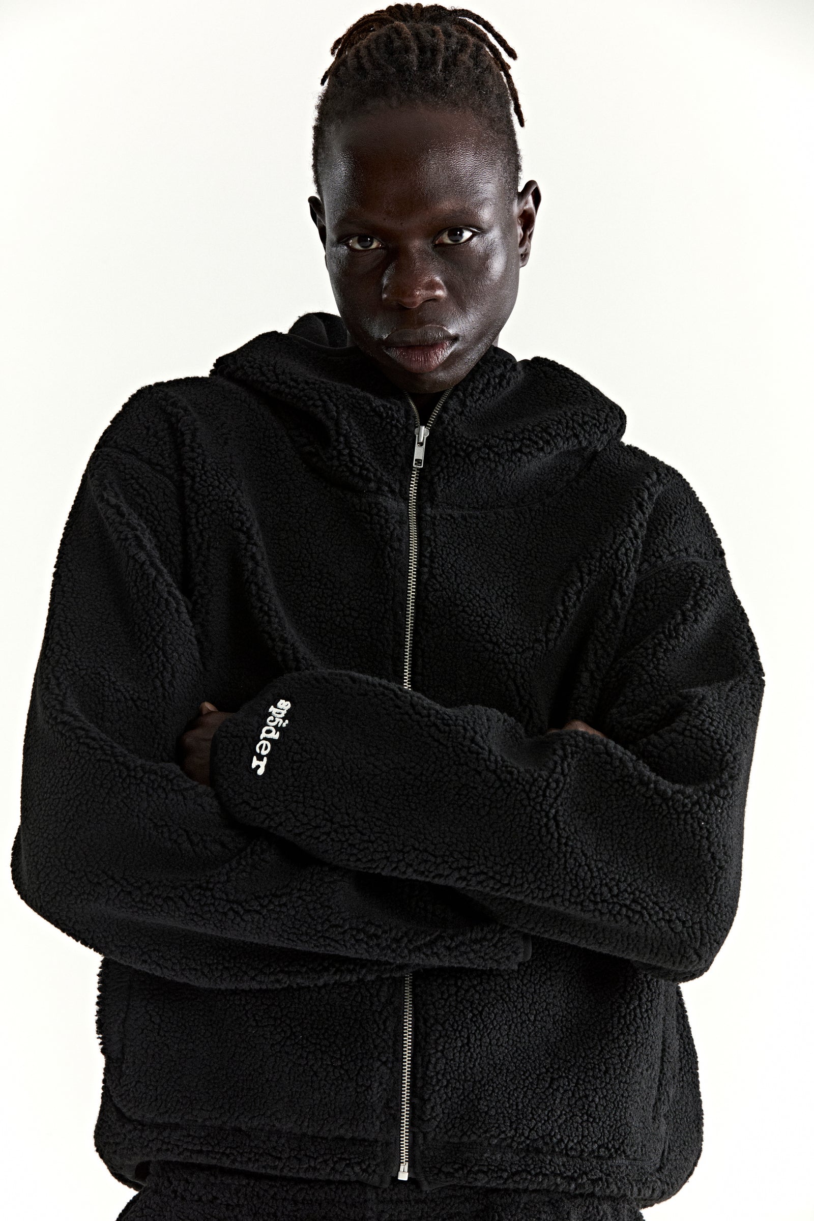 Black teddy fleece zip-up hooded jacket with a rubberized logo patch on the wrist.